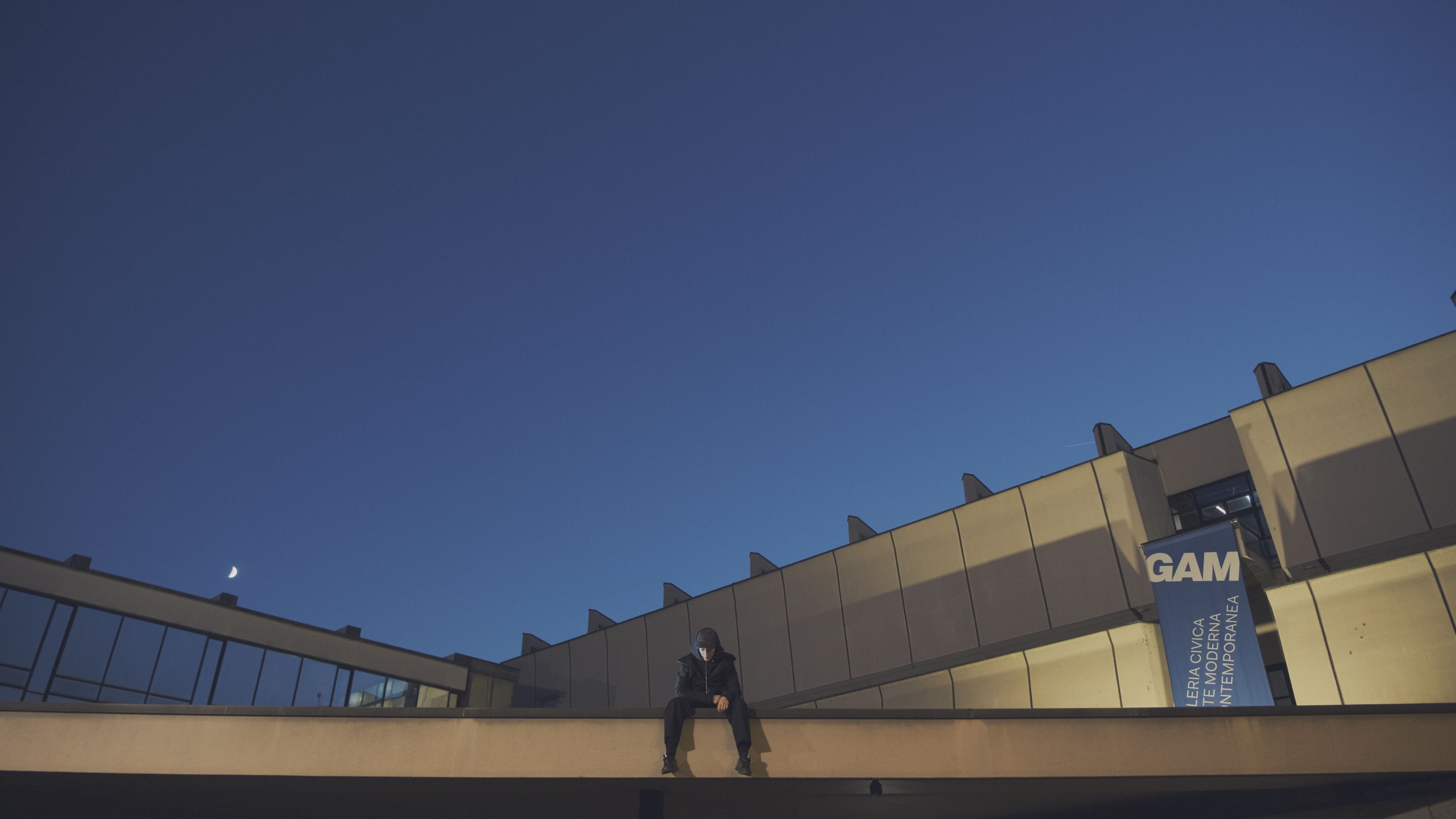 Person sitting on the edge of the GAM museum roof at dusk