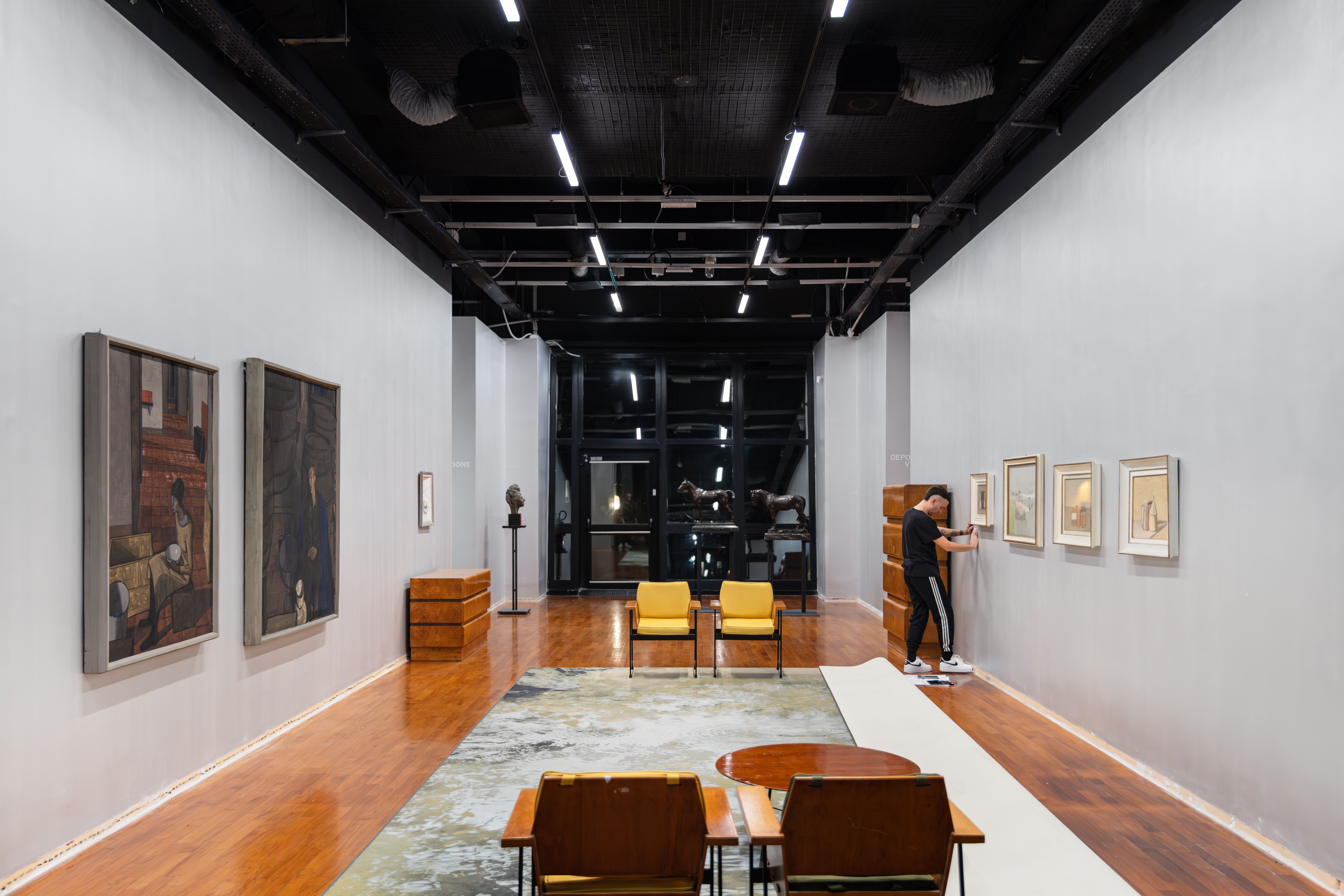 Long museum gallery with paintings and furniture, the artist working at the far wall