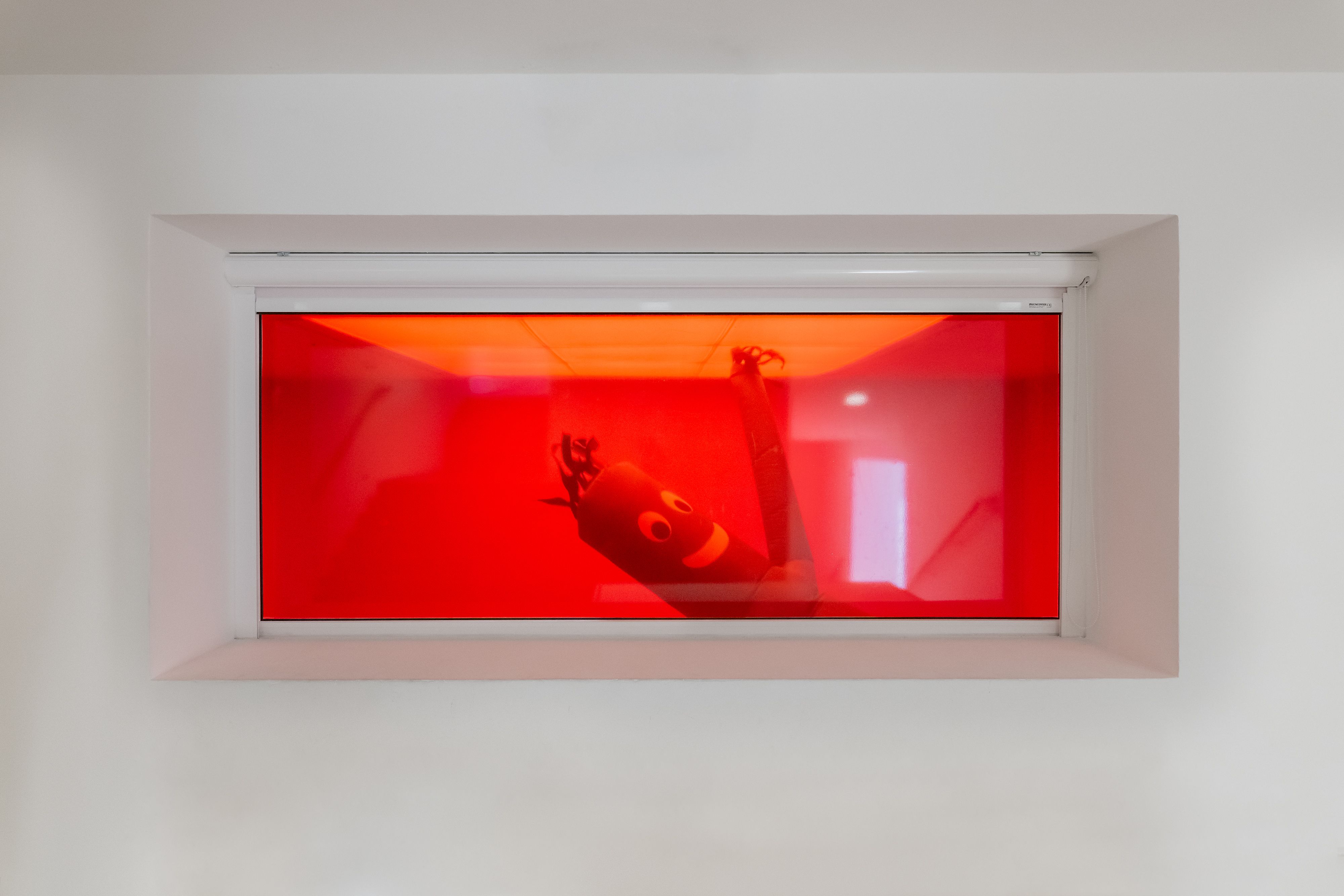 View through a window into a red room with a skydancer inside