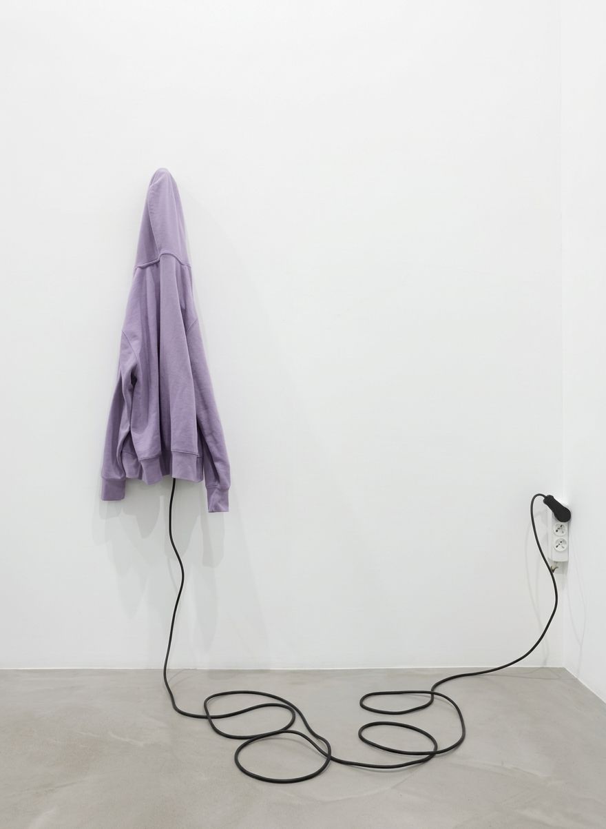 Lilac sweatshirt hung on a white wall, a black cable coiled on the floor