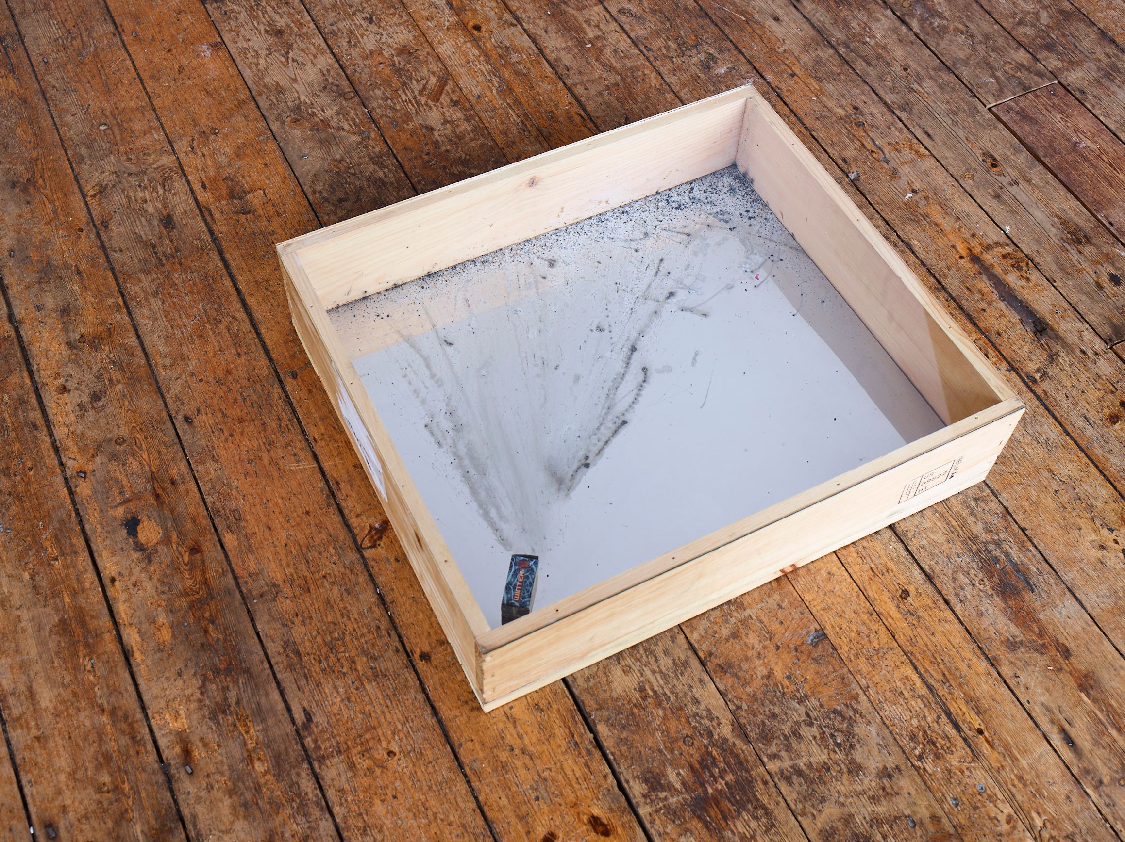 Wooden case on a plank floor with a fan of soot under glass