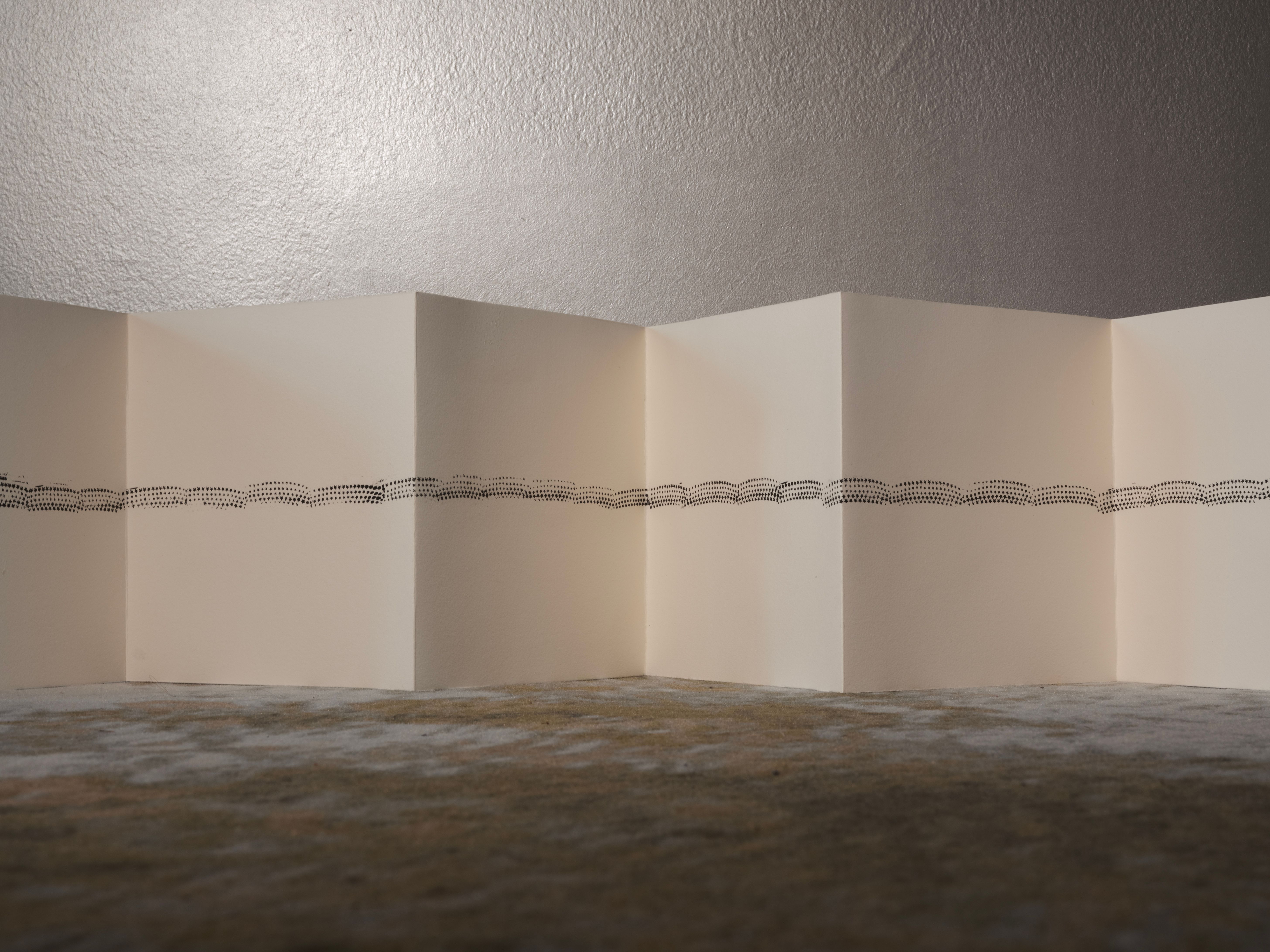 Folded artist's book standing on a carpet against a grey wall