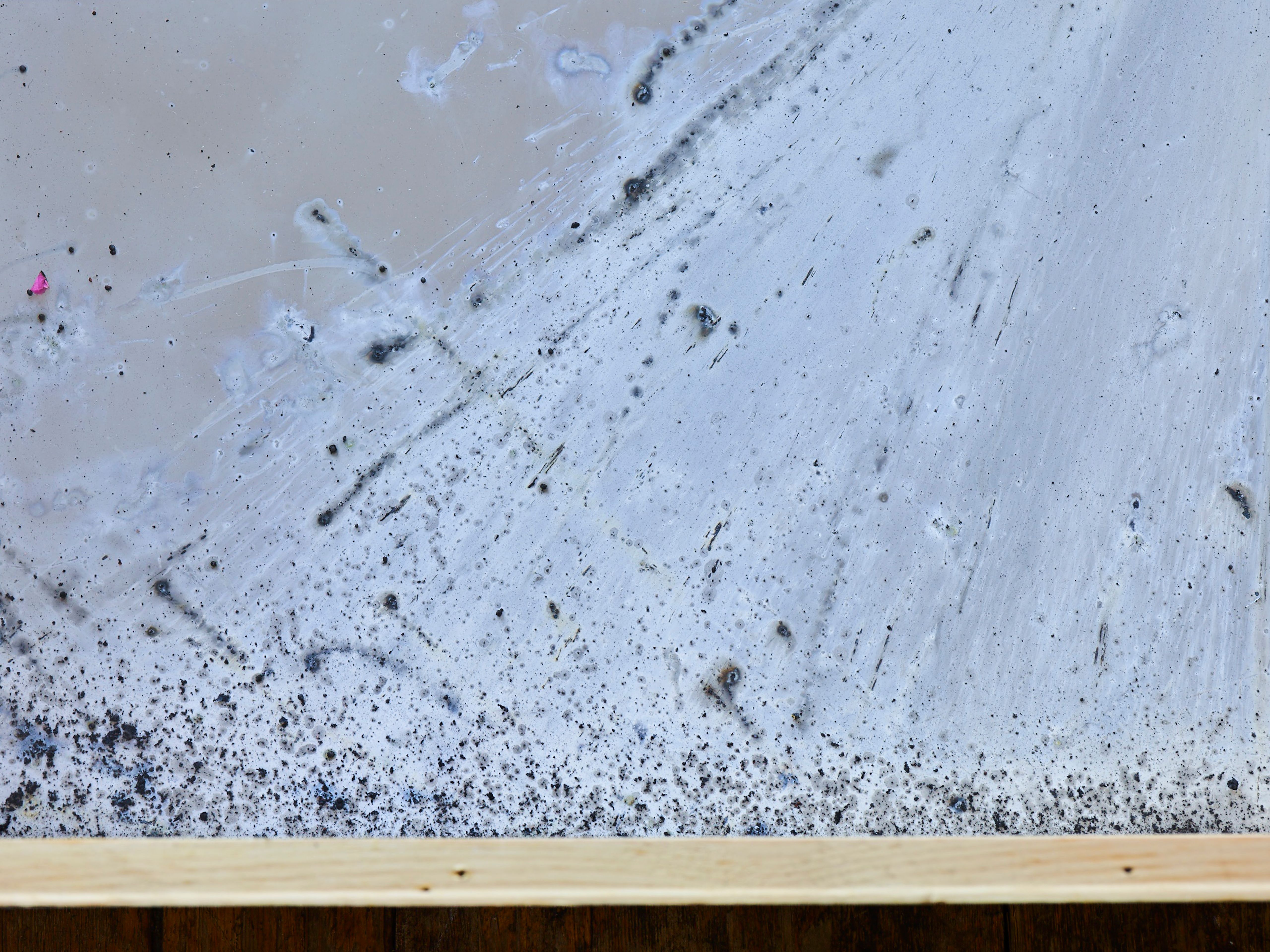 Close-up of soot and firecracker residue on glass inside a wooden frame