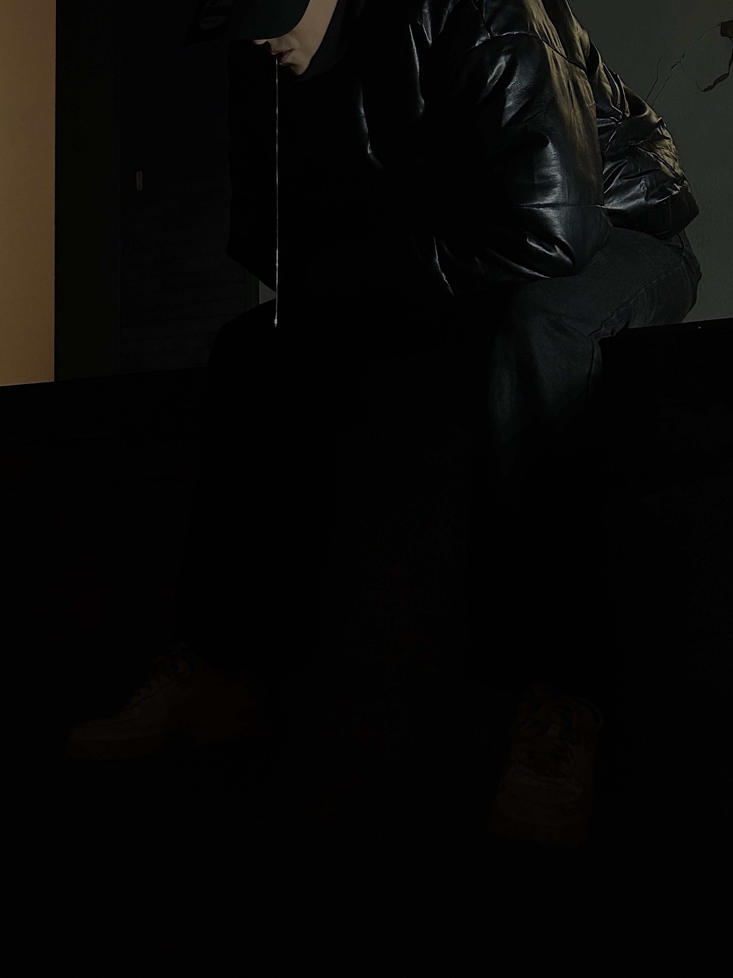 Dark close-up of a seated person in a leather jacket with a thin silver chain from the mouth
