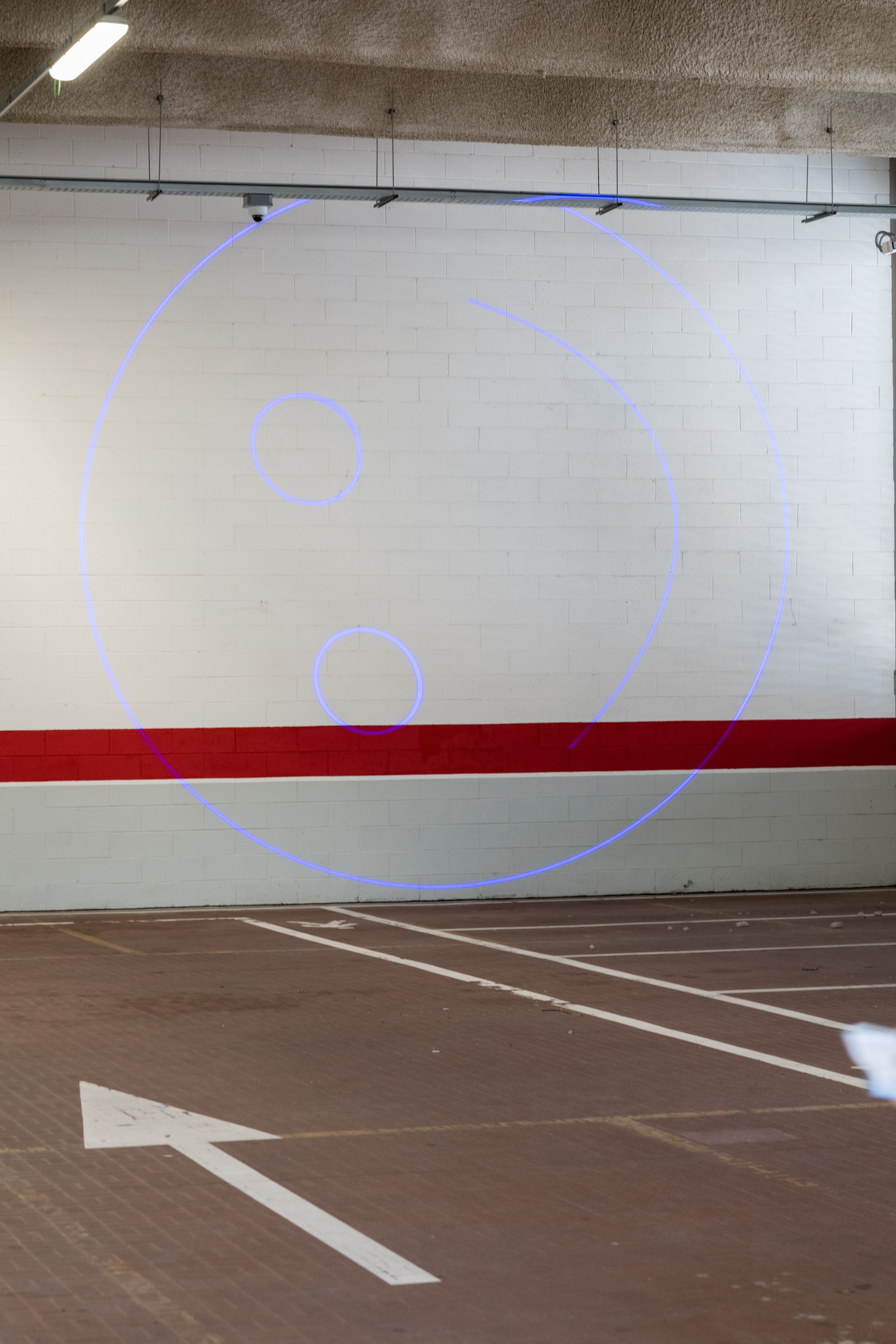Large blue laser smiley on a car park wall above a red stripe