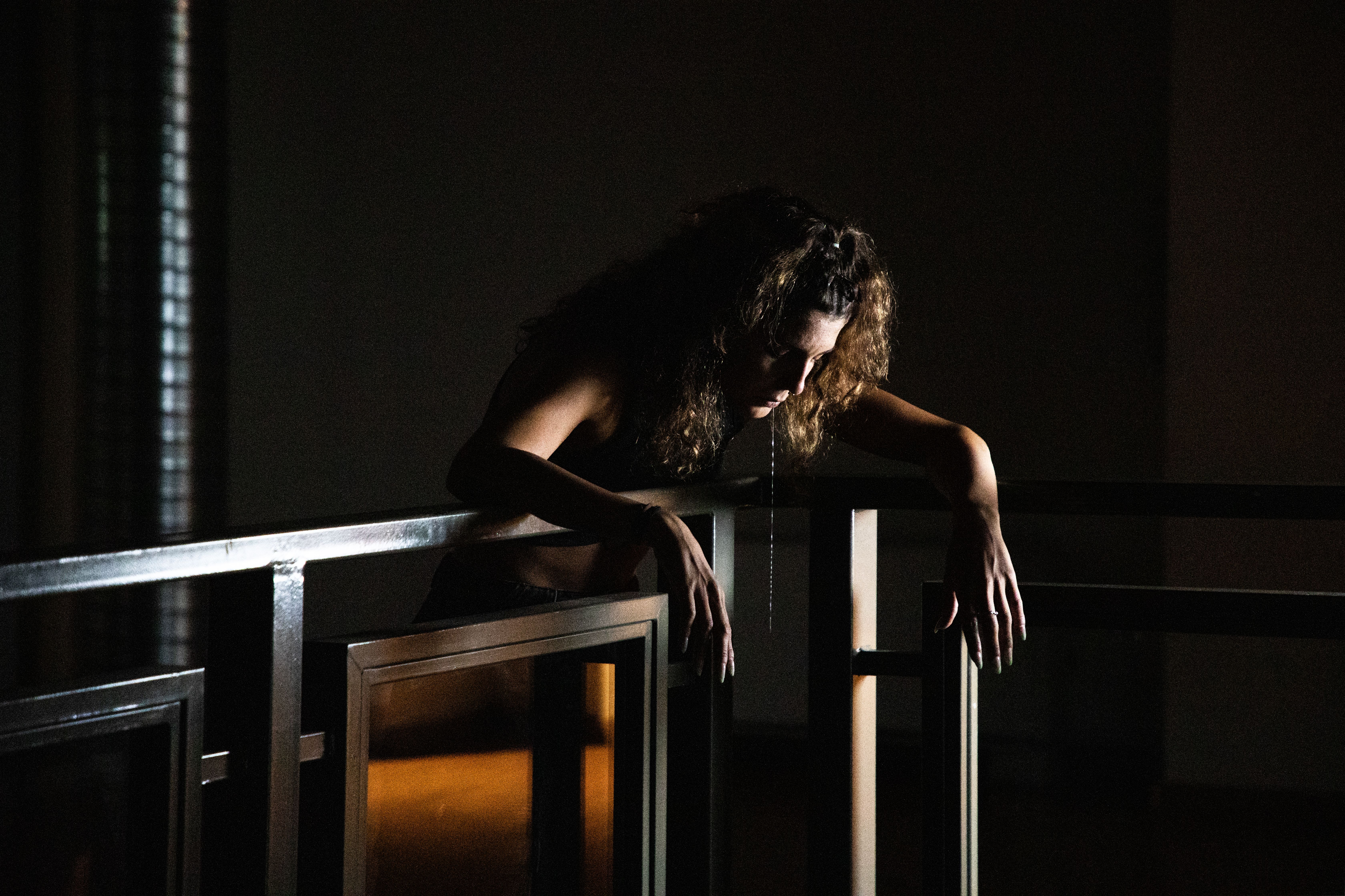 Woman leaning on a railing in the dark, a silver chain hanging from her mouth