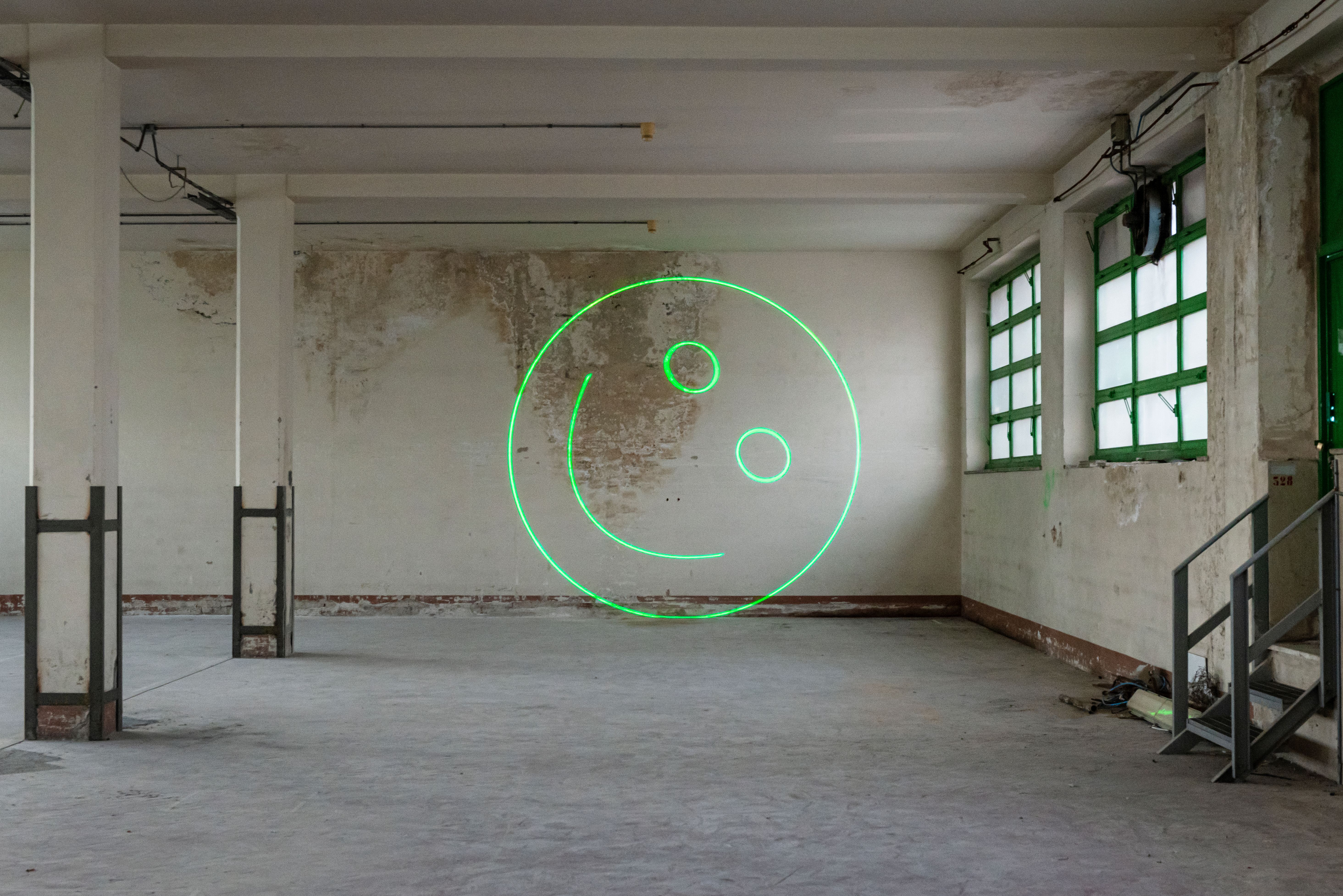 Green laser smiley projected on a worn wall in an empty industrial space