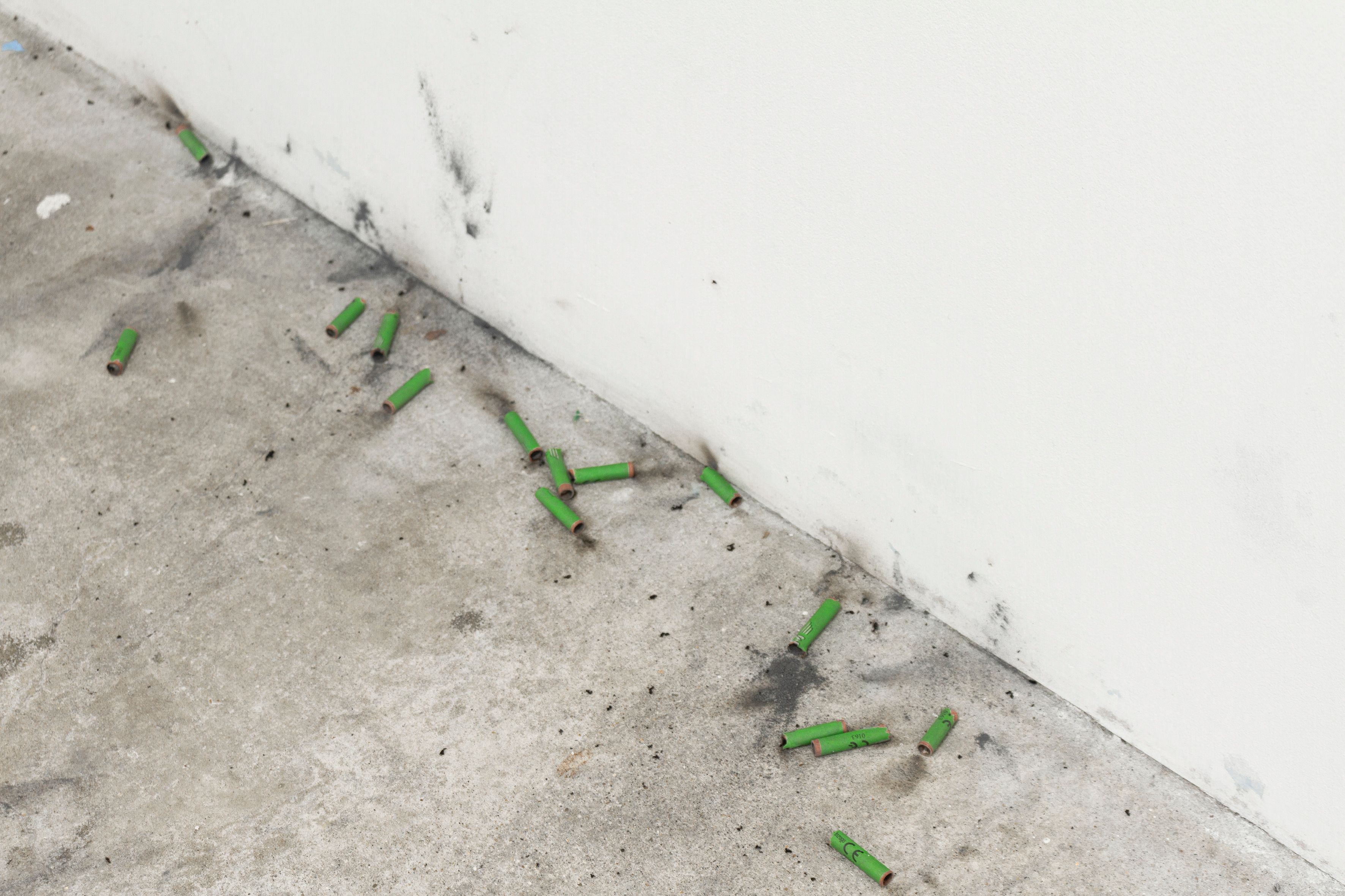 Green spent firecrackers scattered along the base of a white wall