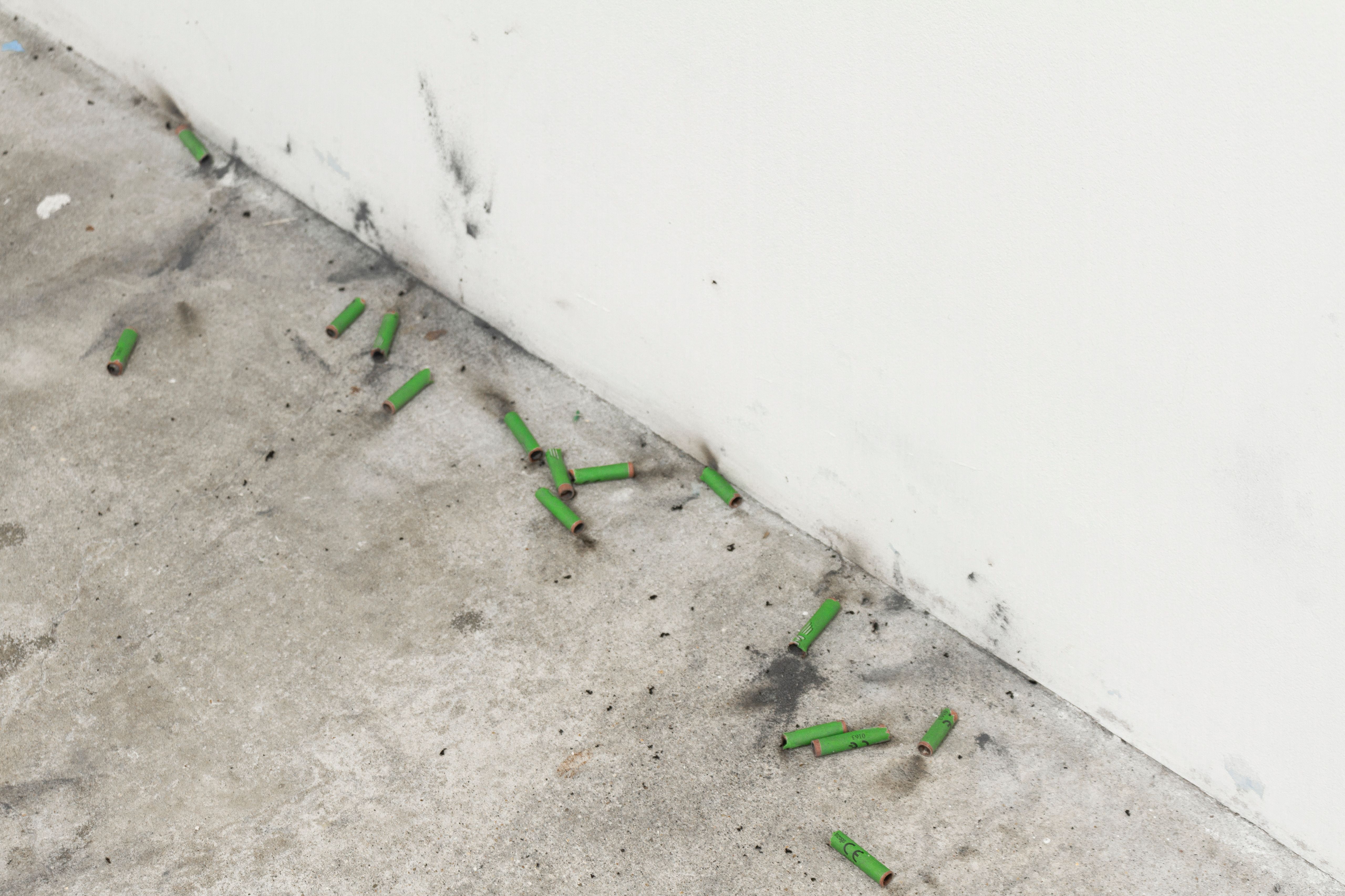 Green spent firecrackers scattered along the base of a white wall
