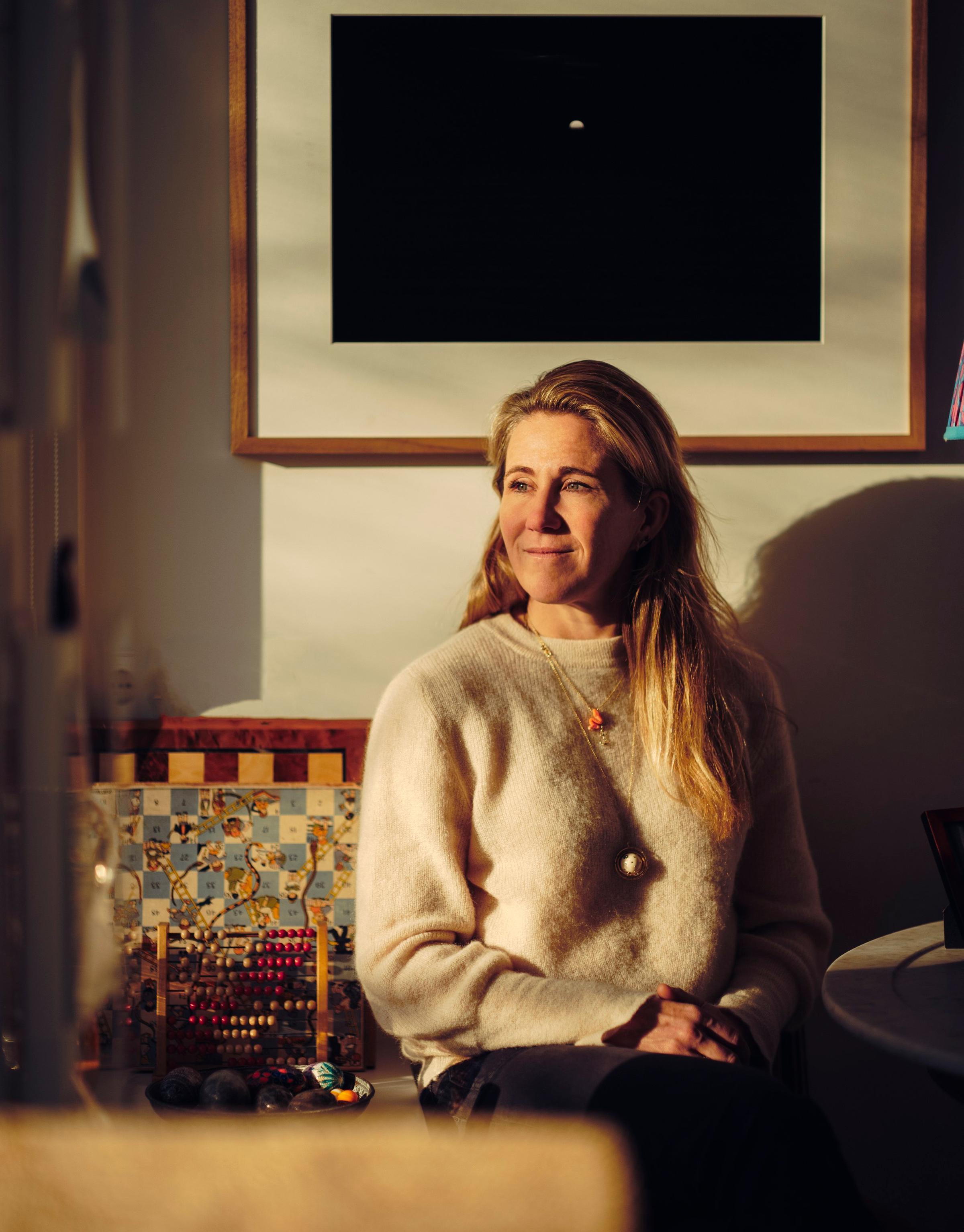A woman with long blonde hair sitting comfortably in a cozy living room, exuding a sense of relaxation and warmth.