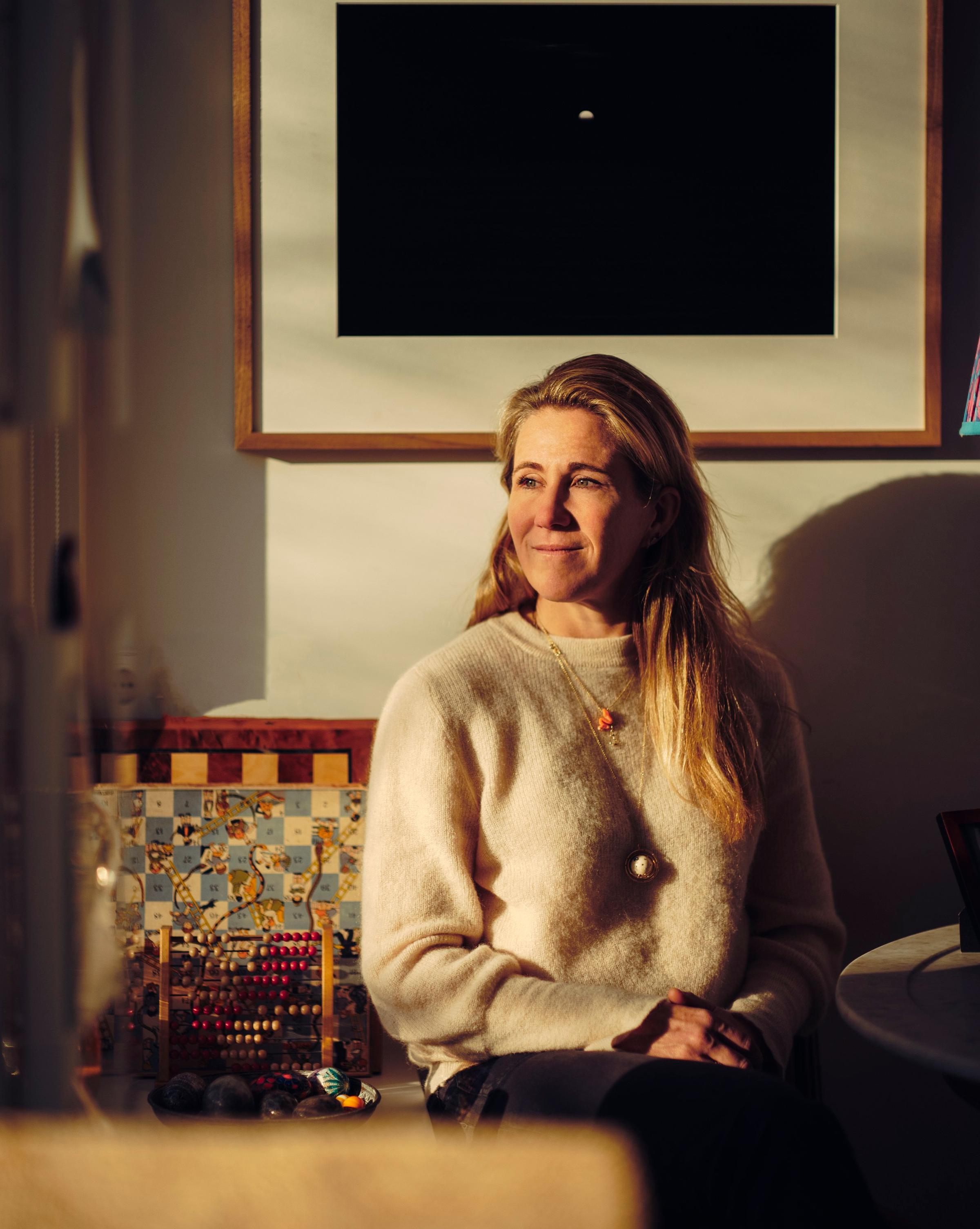 A woman with long blonde hair sitting comfortably in a cozy living room, exuding a sense of relaxation and warmth.