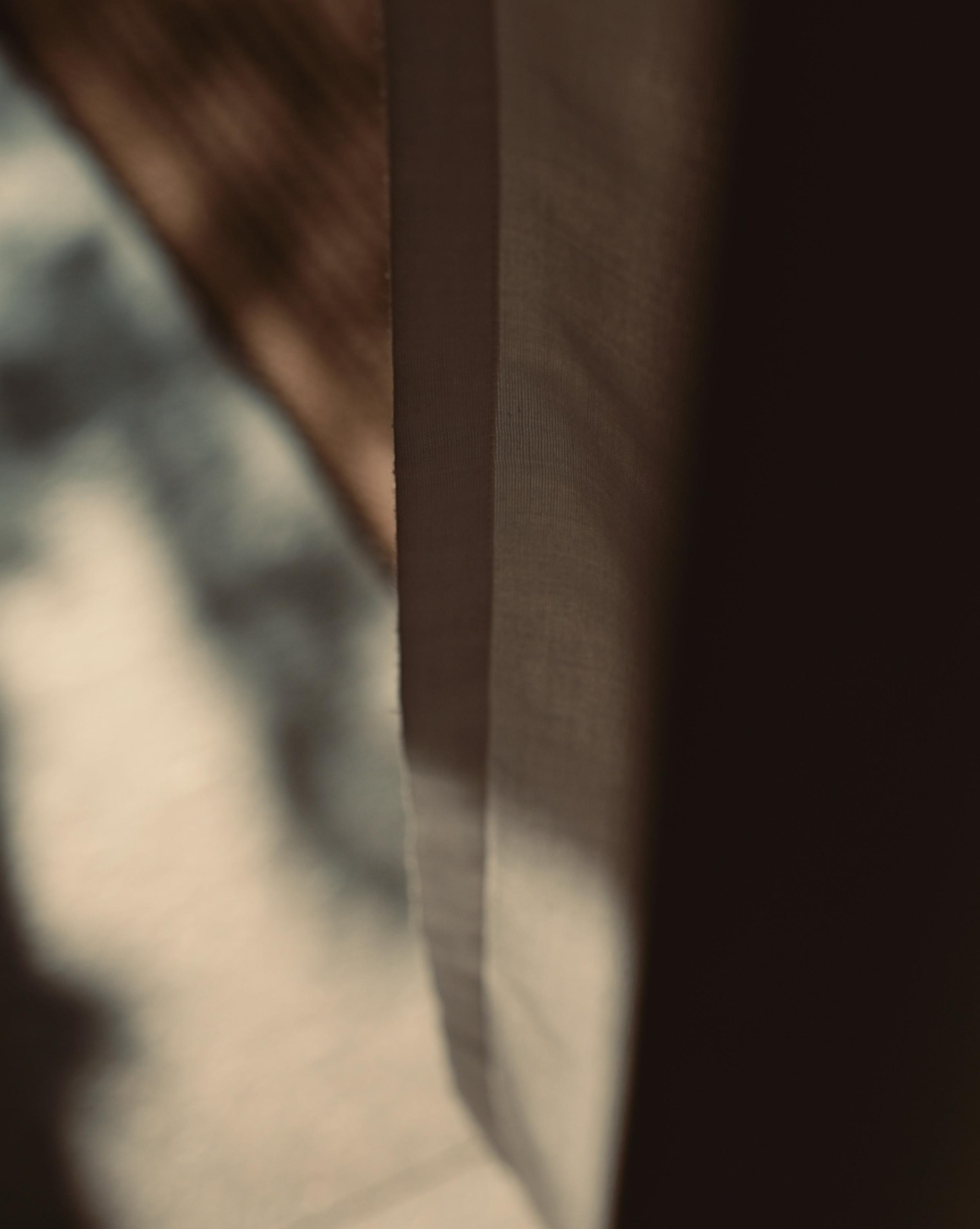 Soft, abstract image showing sunlight filtering through a semi-transparent curtain, casting blurred shadows and warm tones in the background. The scene has a calm, minimalist aesthetic with earthy colors and subtle lighting.