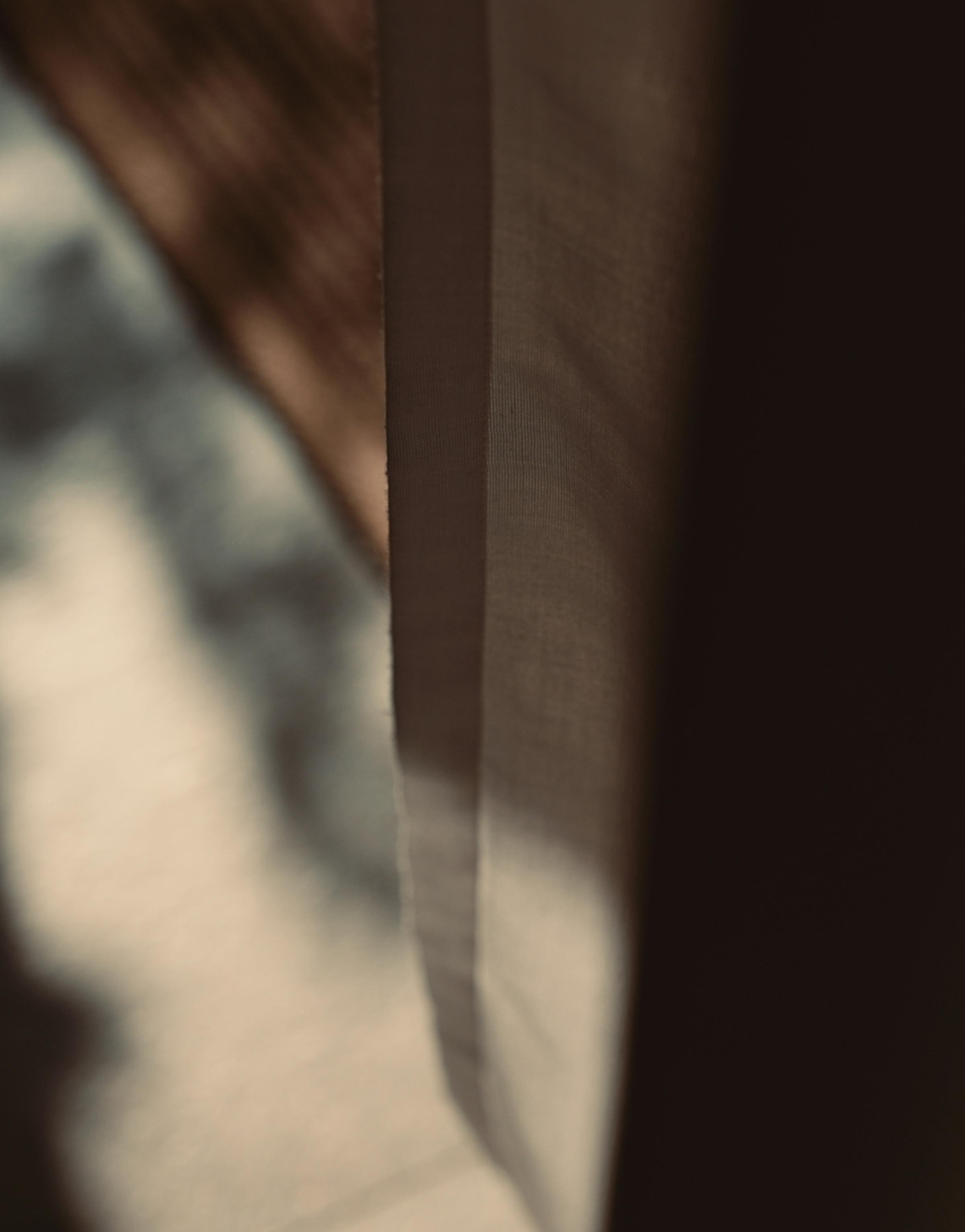 Soft, abstract image showing sunlight filtering through a semi-transparent curtain, casting blurred shadows and warm tones in the background. The scene has a calm, minimalist aesthetic with earthy colors and subtle lighting.