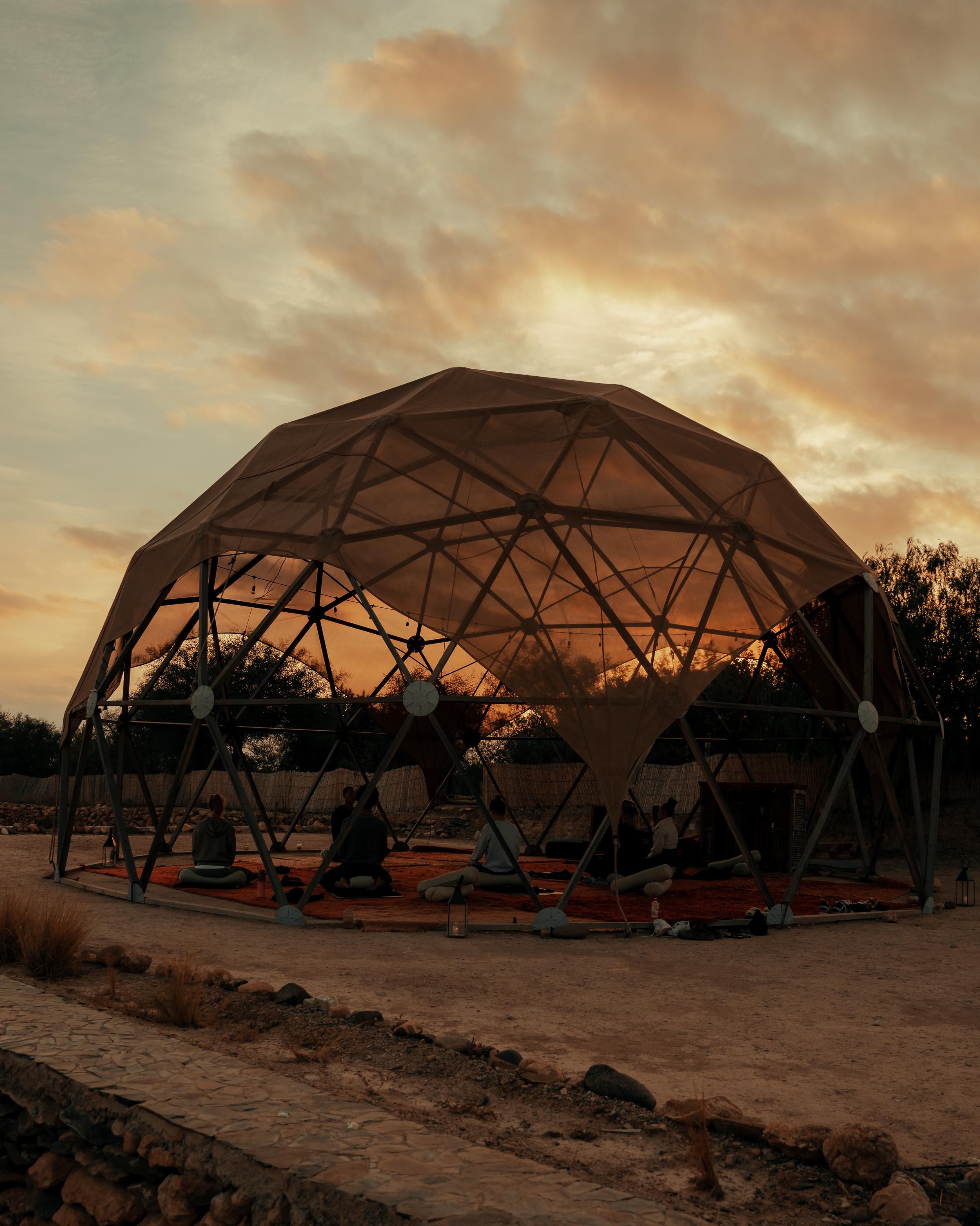 A dark desert landscape with a hint of yellow in the sky, with the yoga dome in the middle.