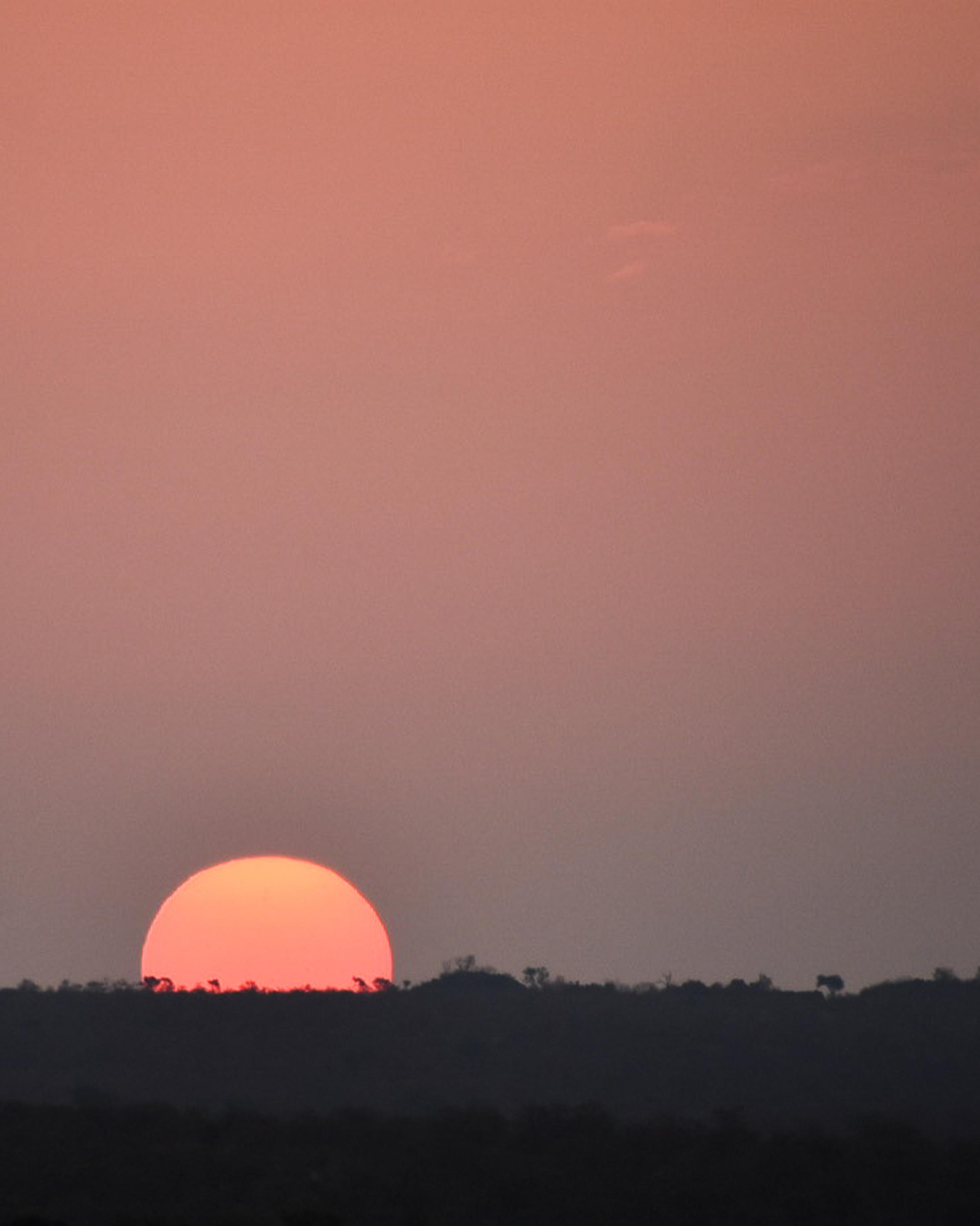 A stunning sunset or sunrise with the sun appearing in vibrant orange-red hues, casting a warm glow across the sky