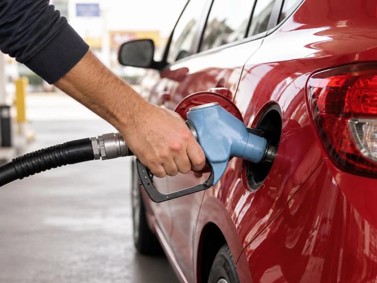 A person pumps gas into a red car at a gas station.