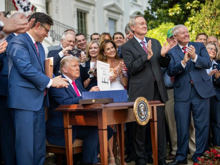 Donald Trump holds up the signed One Big Beautiful Bill Act while Republican lawmakers applaud outside the White House.