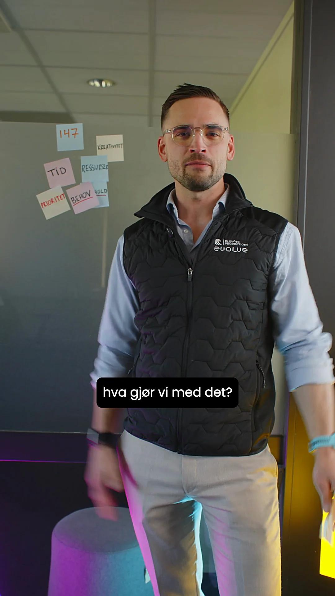 Mann med briller og vest ser i kamera foran en vegg med gule lapper