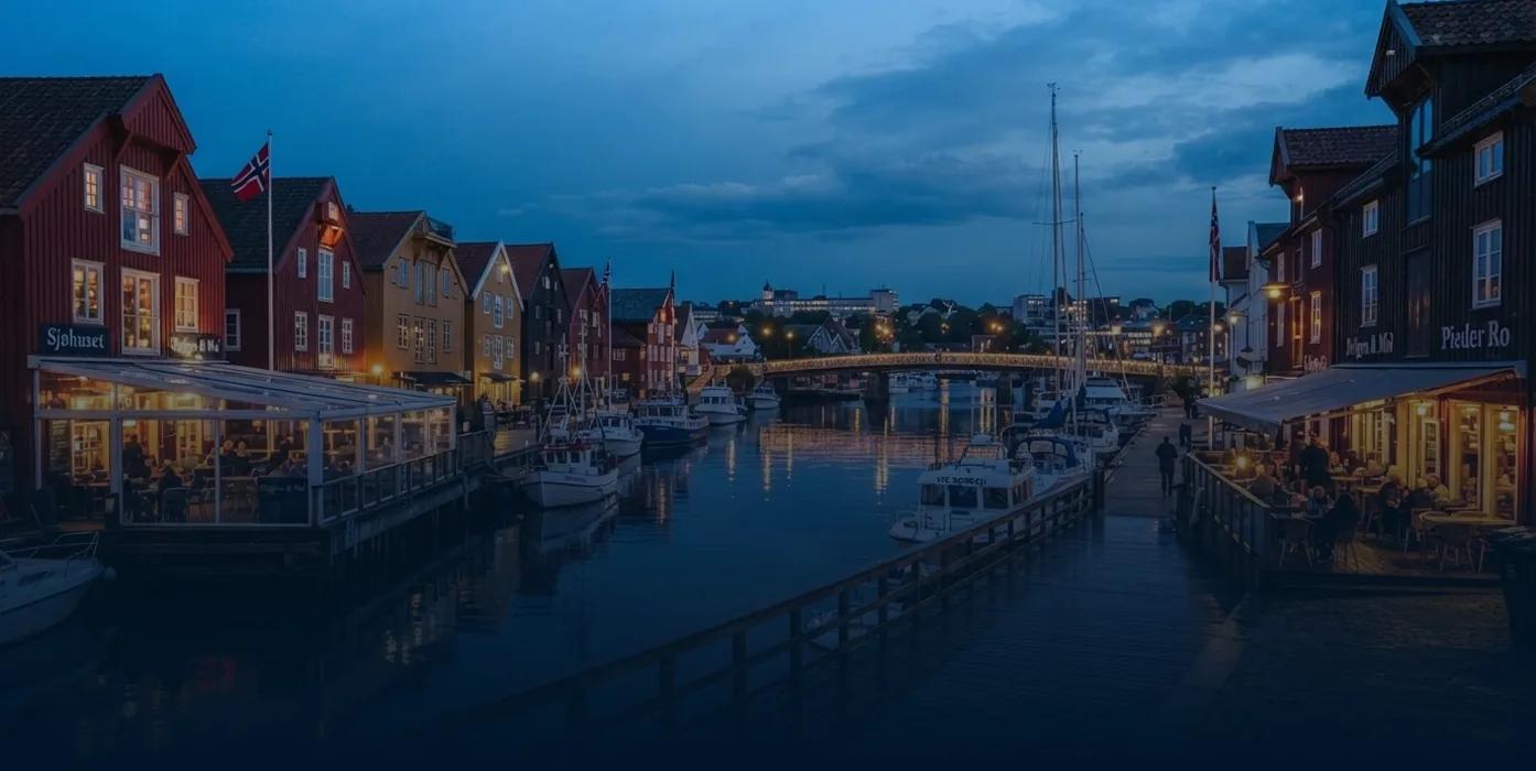 Fiskebrygga i Kristiansand om kvelden med båter og opplyste restauranter