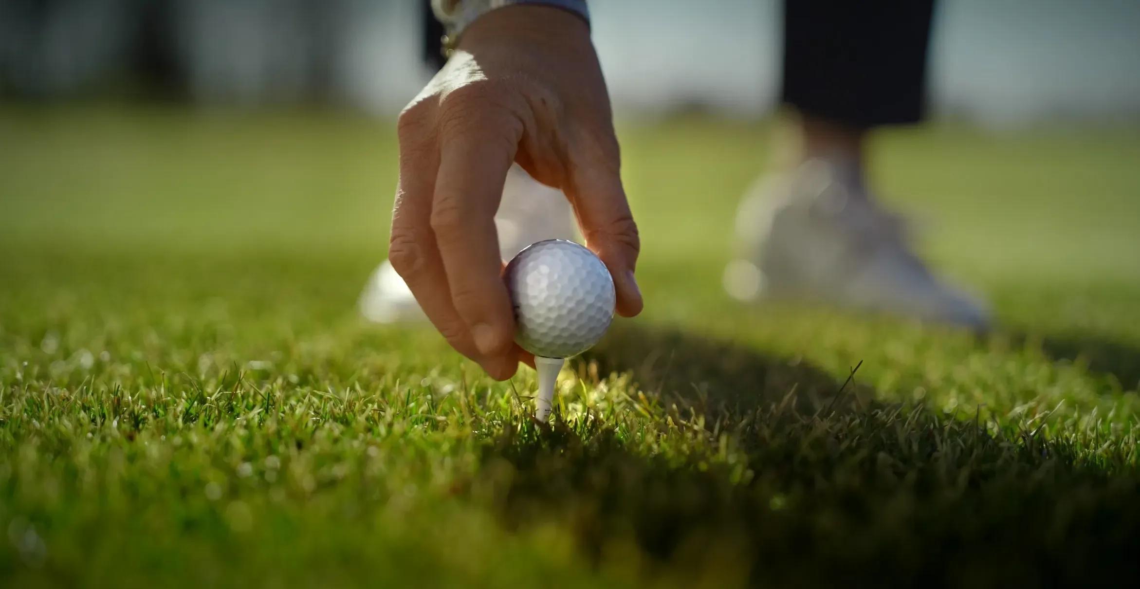 Hånd setter en golfball på tee på gresset