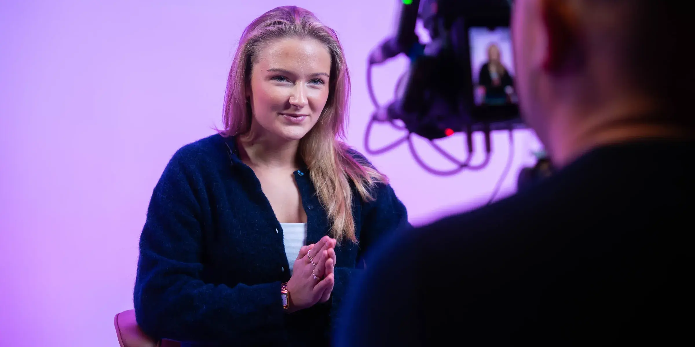 Ung kvinne blir intervjuet foran lilla bakgrunn, filmet over skulderen på kameraoperatøren