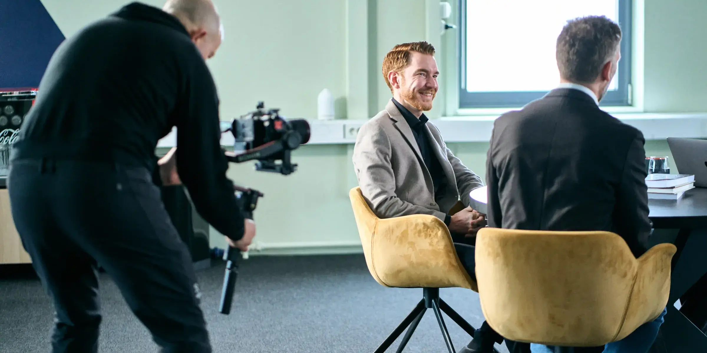 Kameraoperatør med gimbal filmer to menn i samtale i et møterom