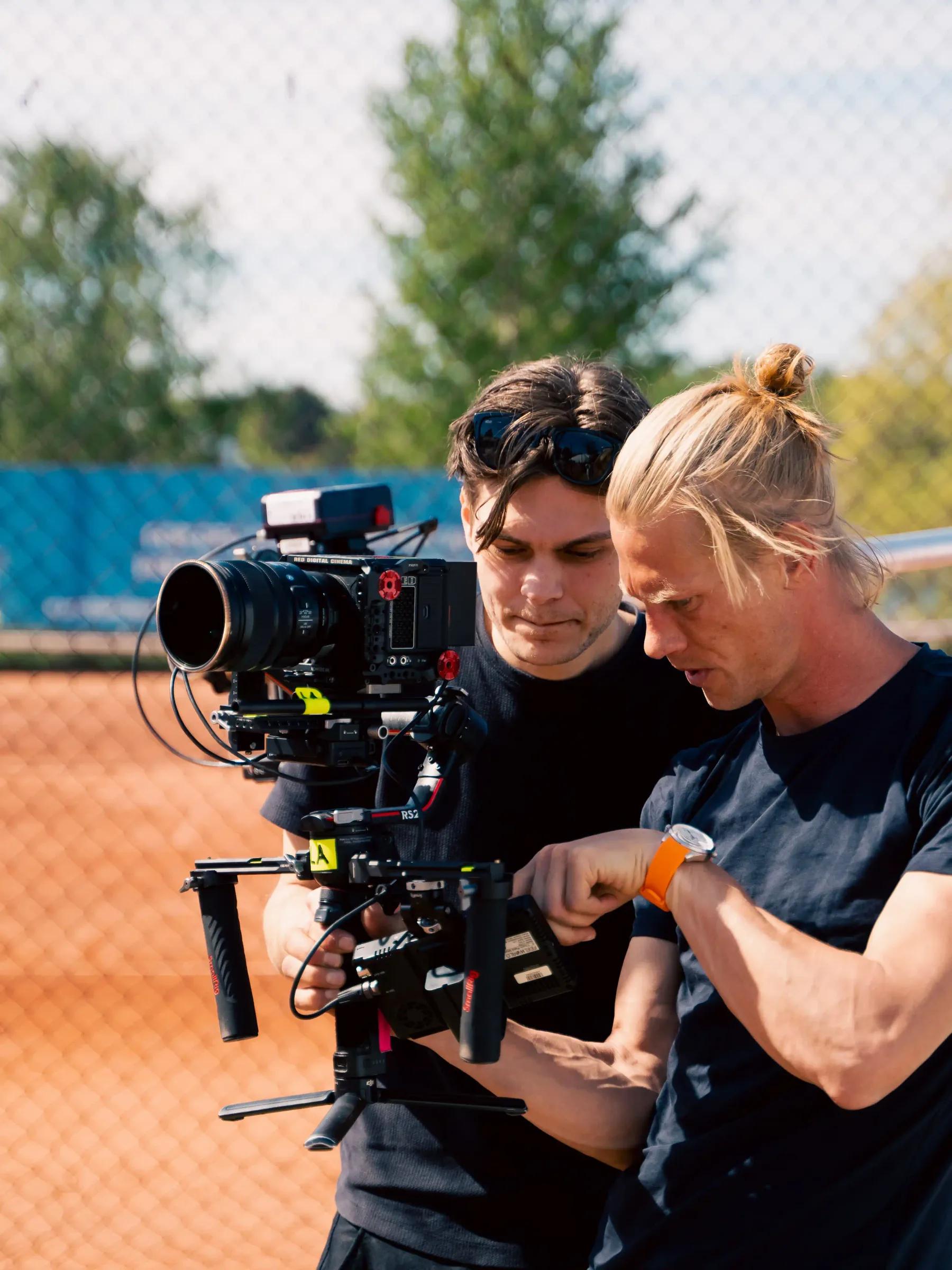 To kameraoperatører gjør klar et filmkamera på en tennisbane