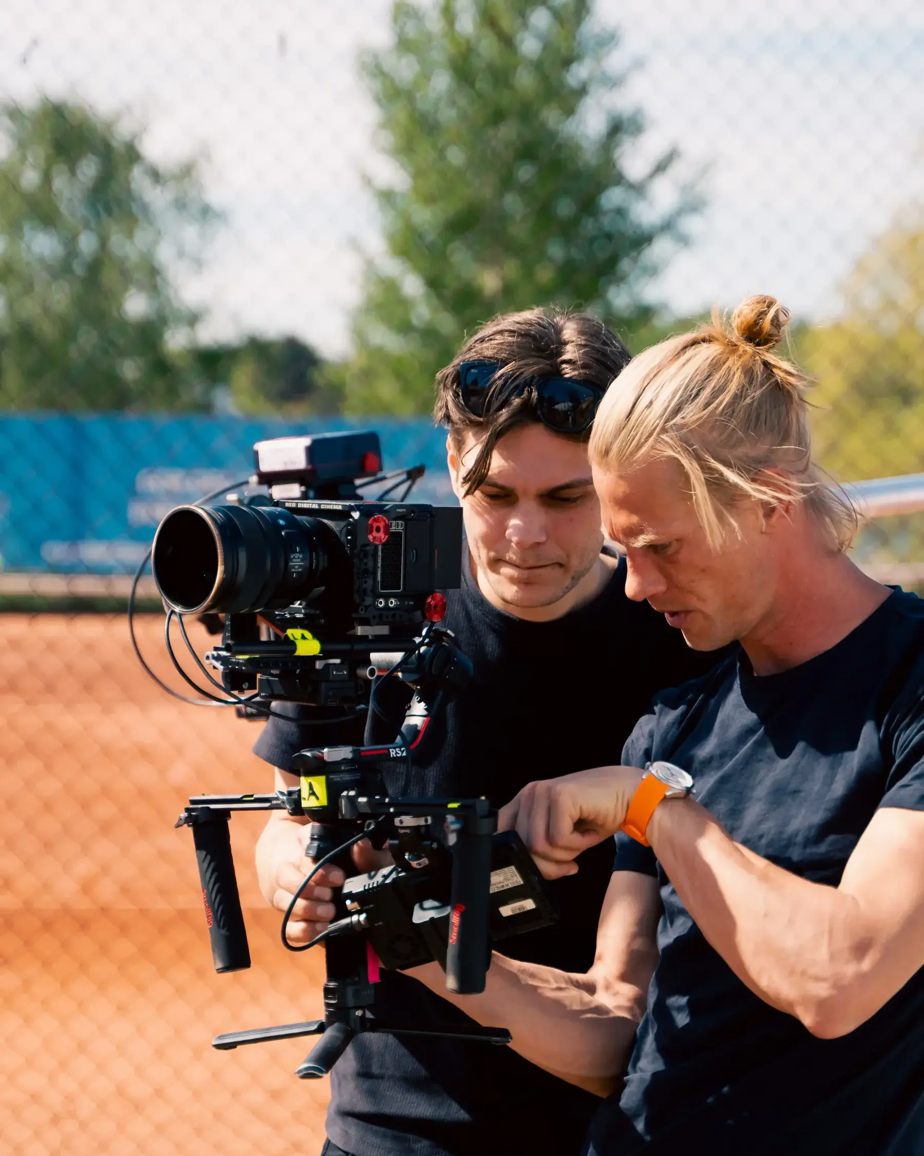 To kameraoperatører gjør klar et filmkamera på en tennisbane