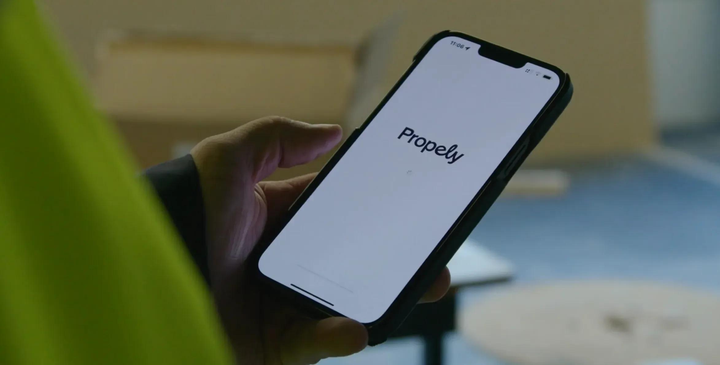 Hånd holder en mobil med Propely-appen åpen