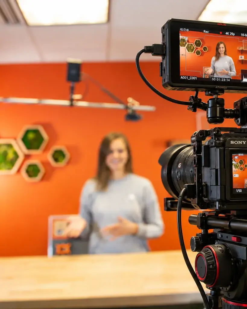 Kamera med skjerm filmer en presentatør foran en oransje vegg i et studio