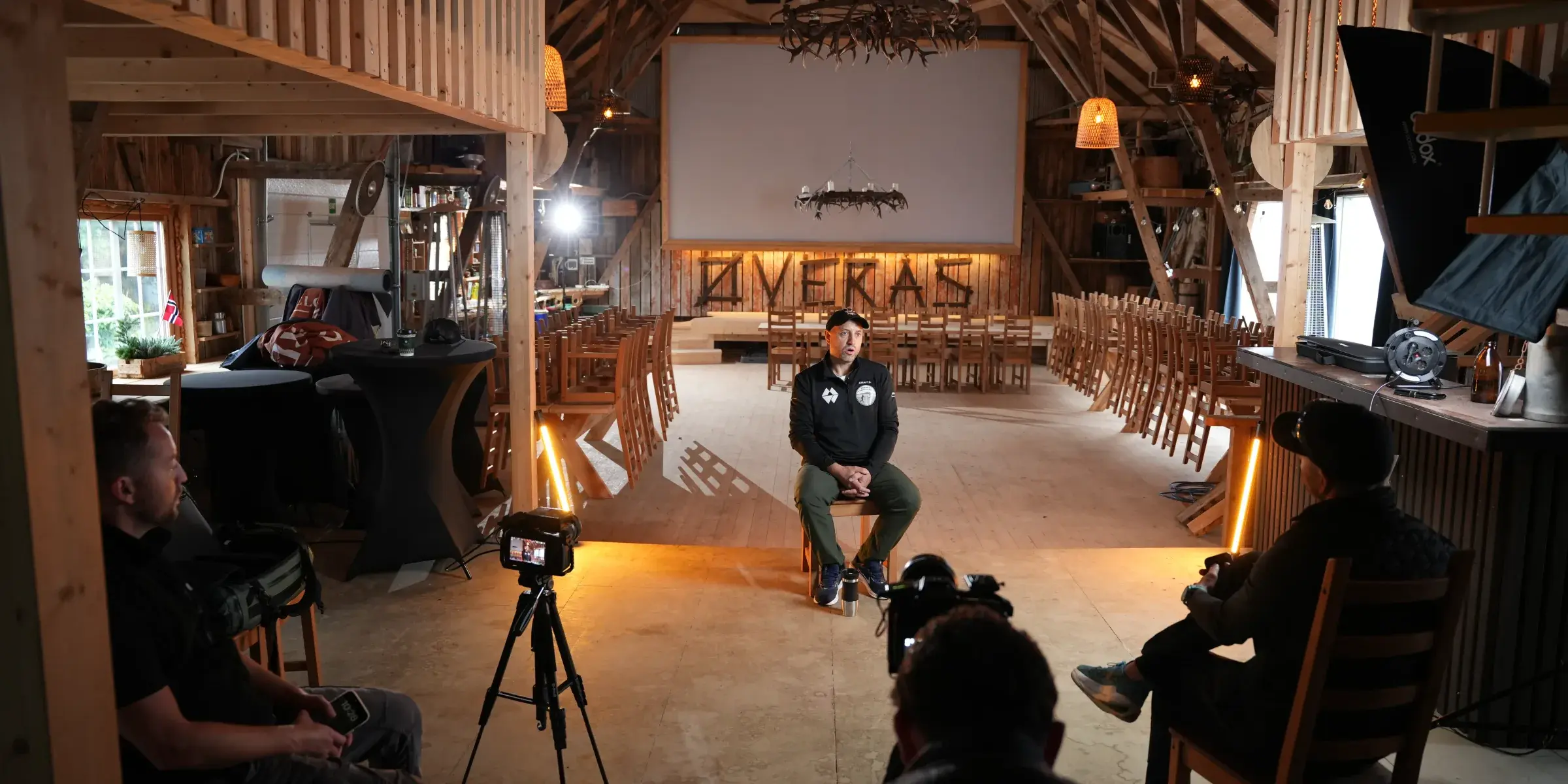 Intervju filmes i en ombygd låve med varmt lys og filmteam i forgrunnen