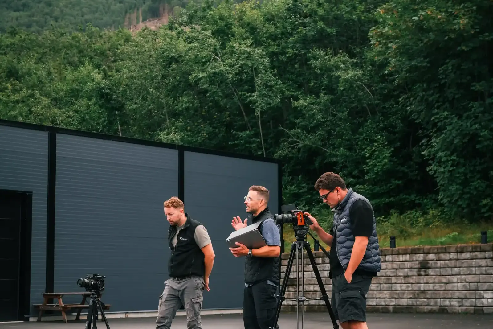 Filmteam med kamera og stativ under et utendørs opptak ved en grønn fjellside