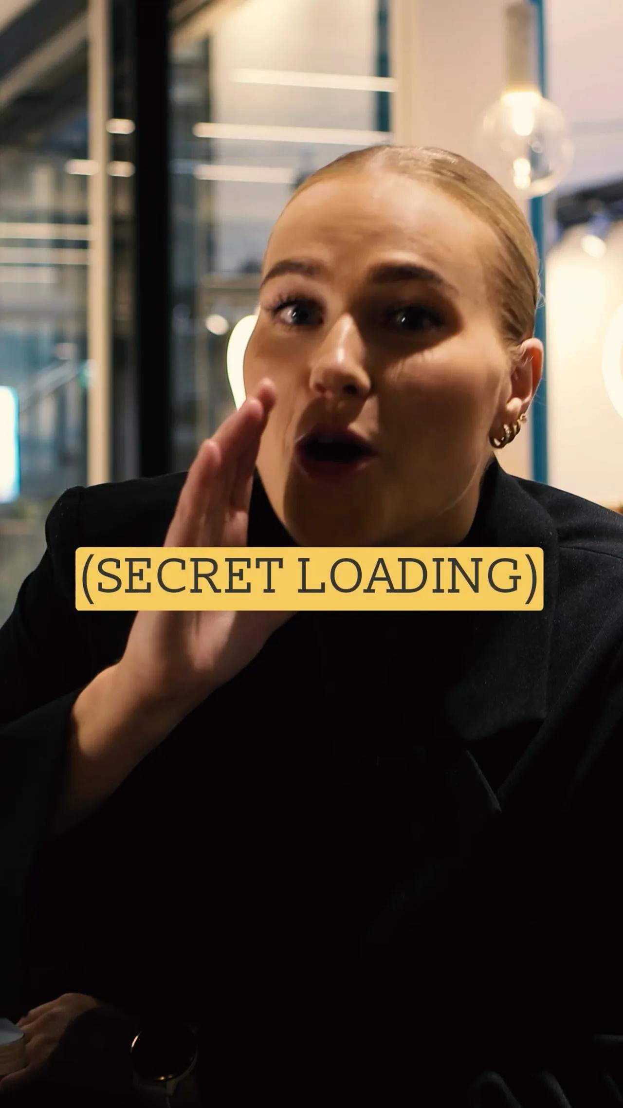 Kvinne holder hånden ved munnen og hvisker til kamera med teksten «Secret loading»