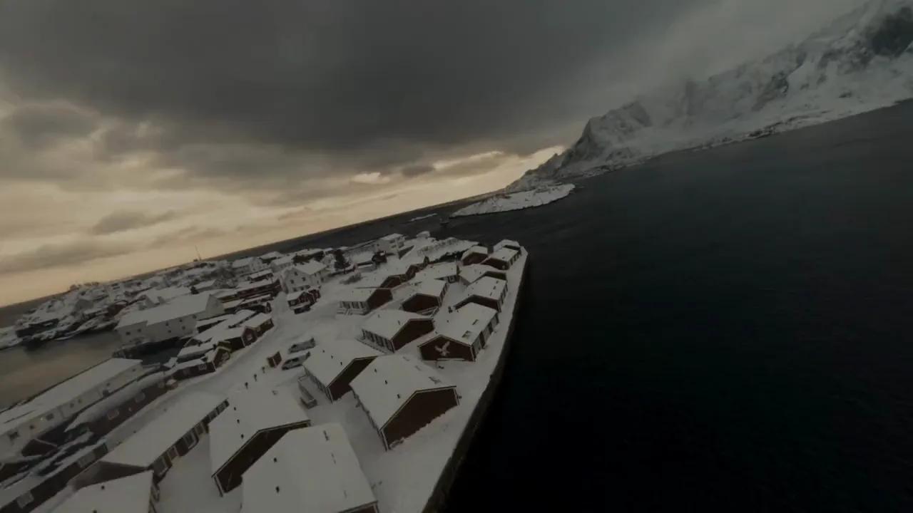 Dronebilde av snødekte rorbuer ved en mørk fjord