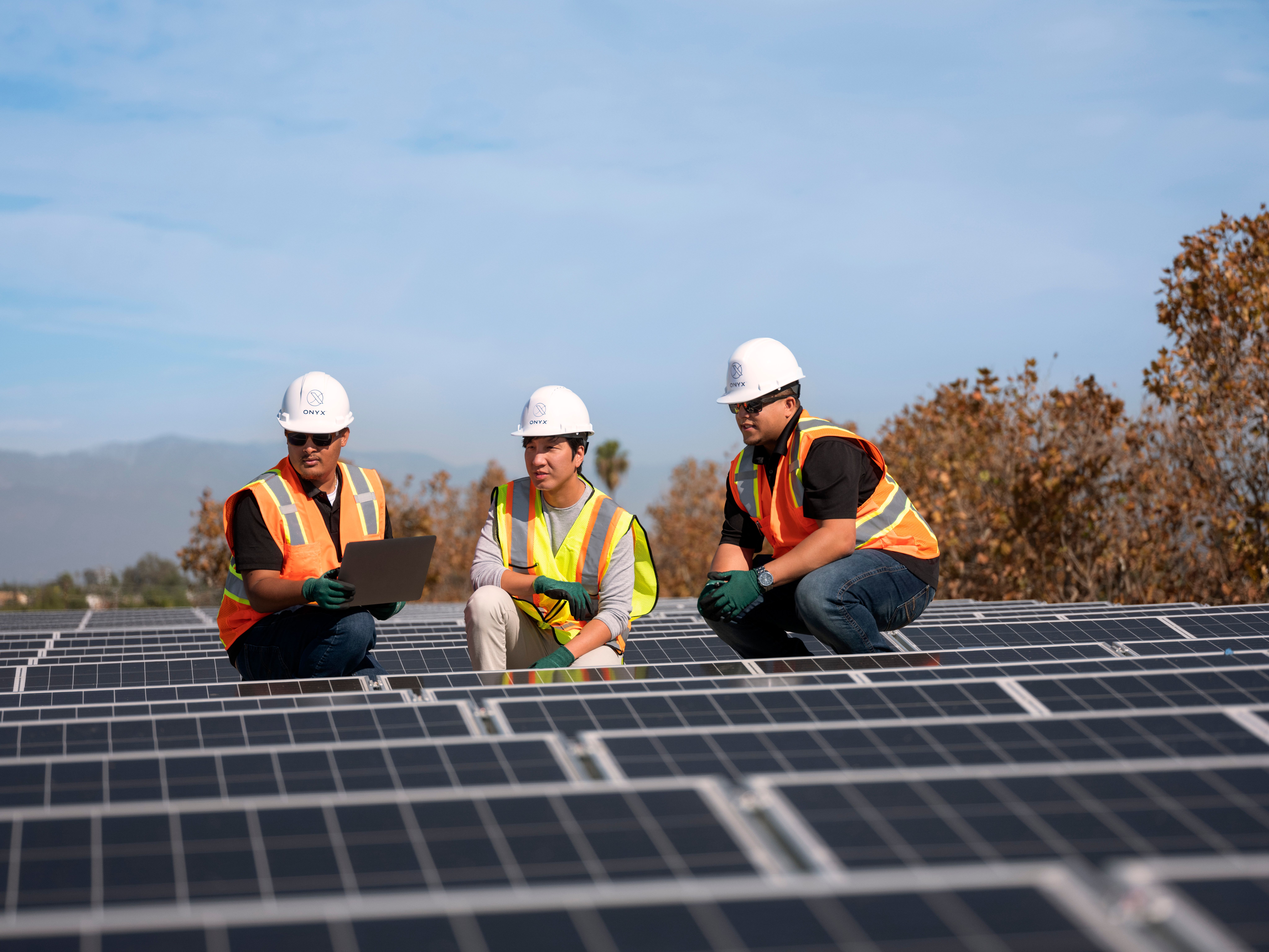 three men kneeling and observing solar panel site