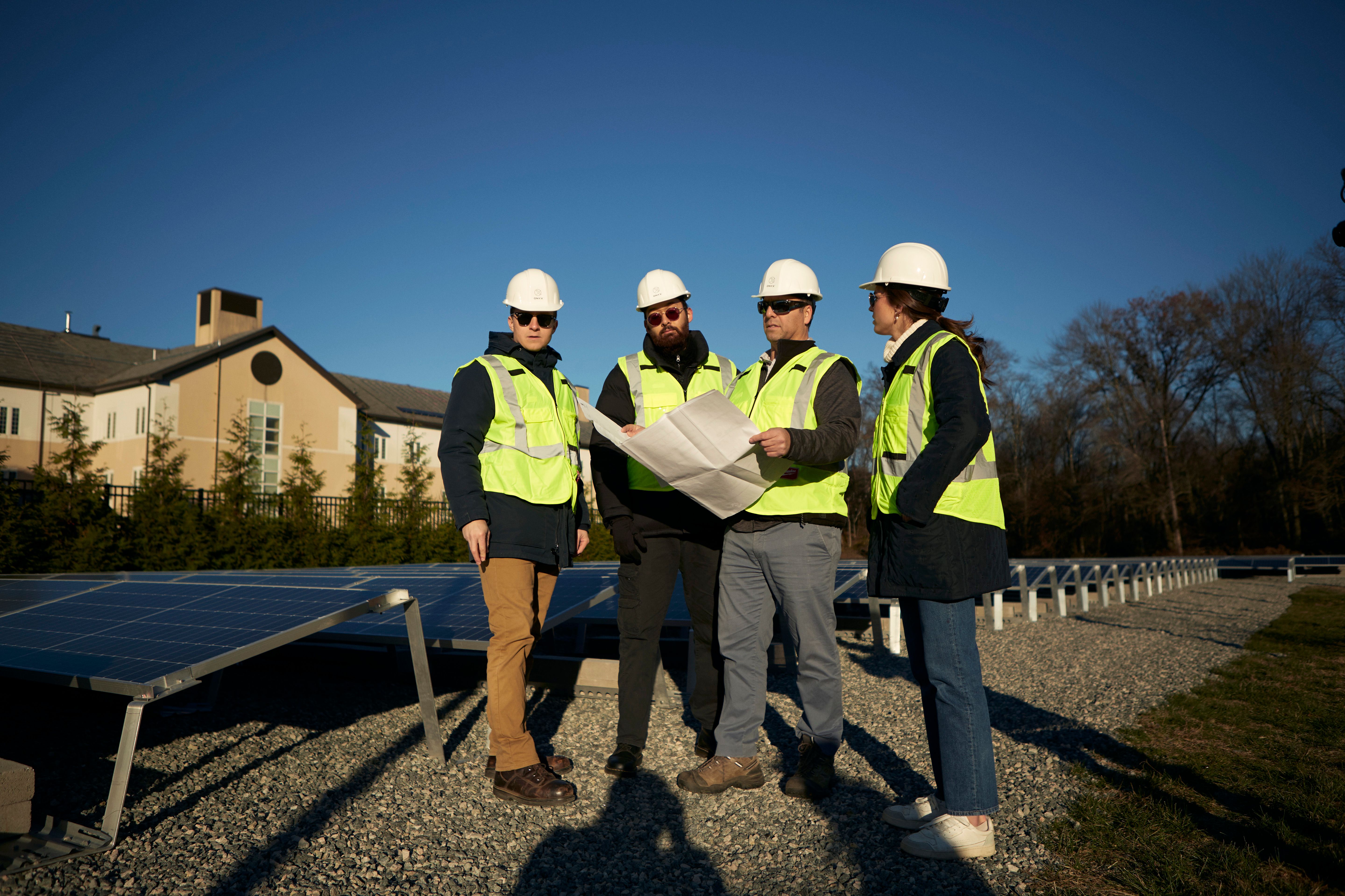 Four workers discussing and reviewing plans for solar energy project - Onyx Renewables