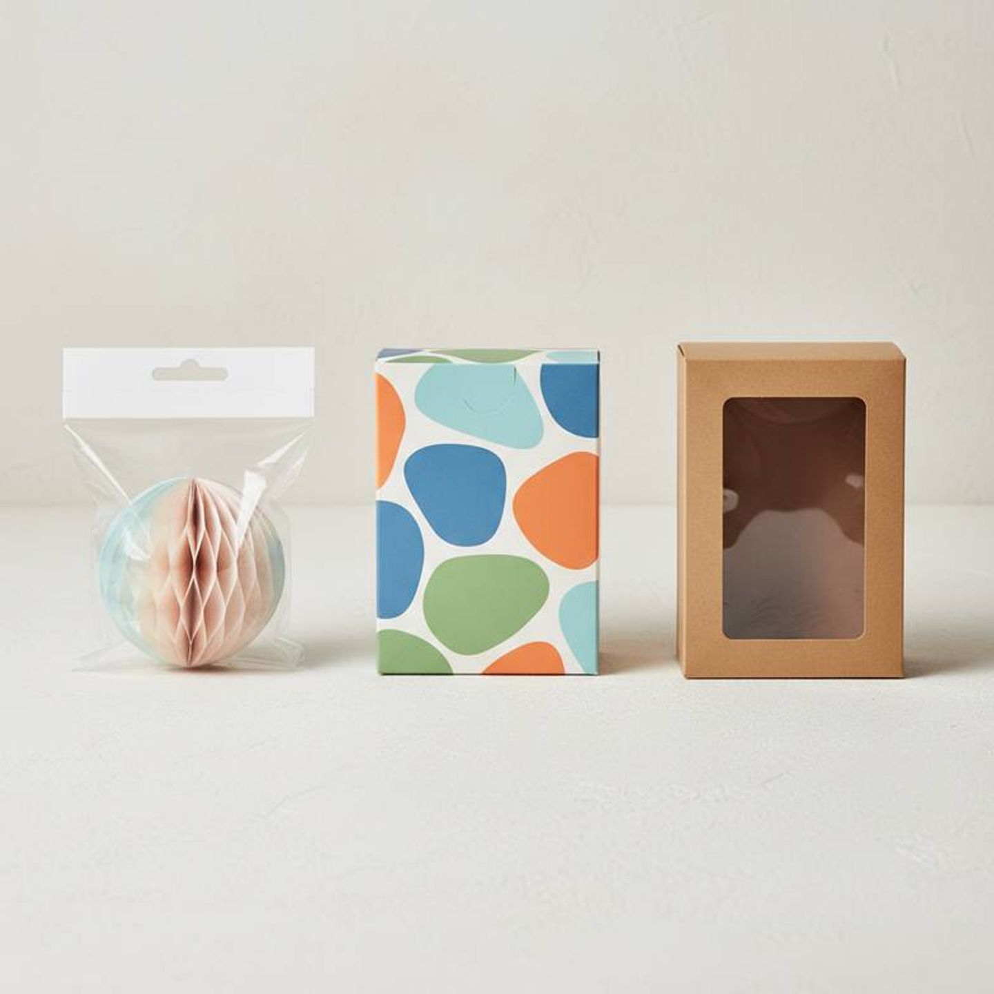 A flat lay of different packaging materials: a clear polybag, a folded color box, and a rigid window box.