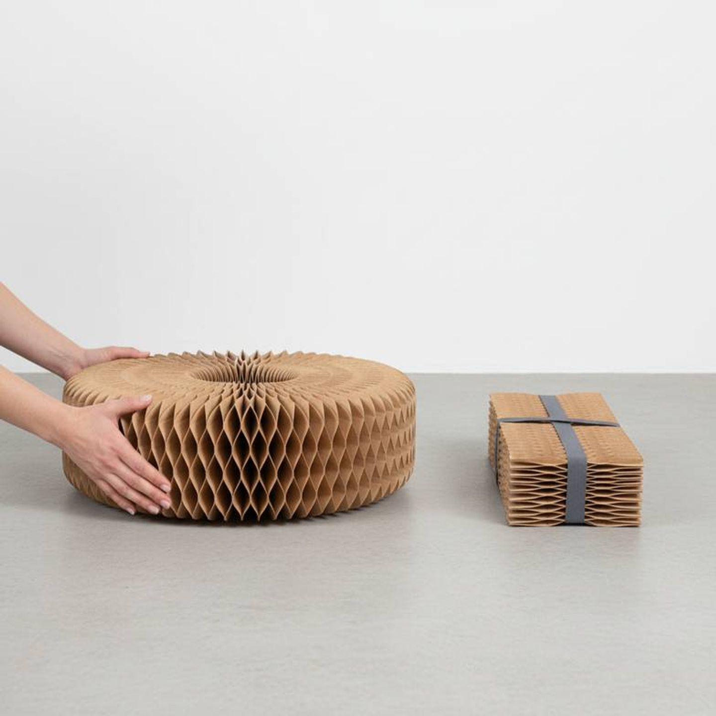 A person easily folding down a honeycomb paper bench for compact storage.