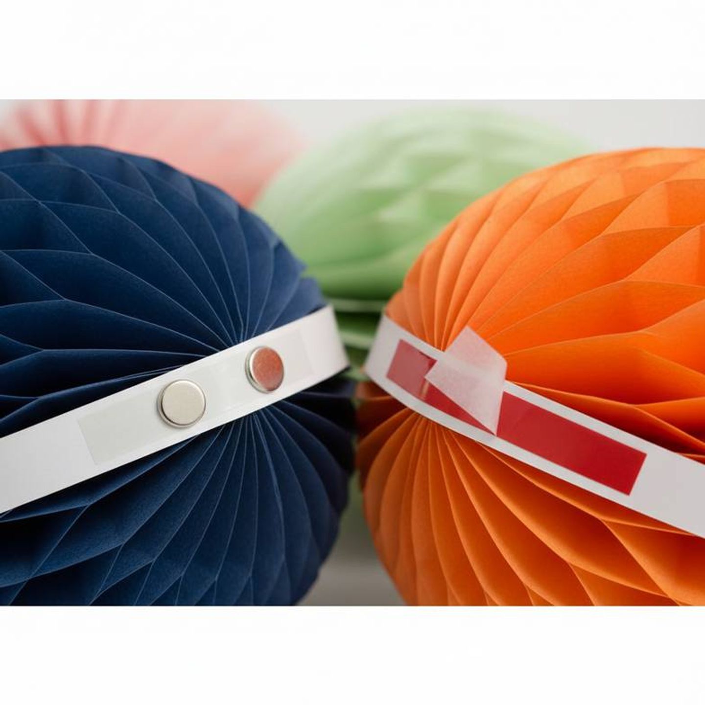 A close-up showing two closure types on honeycomb paper decorations: one with small embedded magnets and another with a peel-off adhesive strip