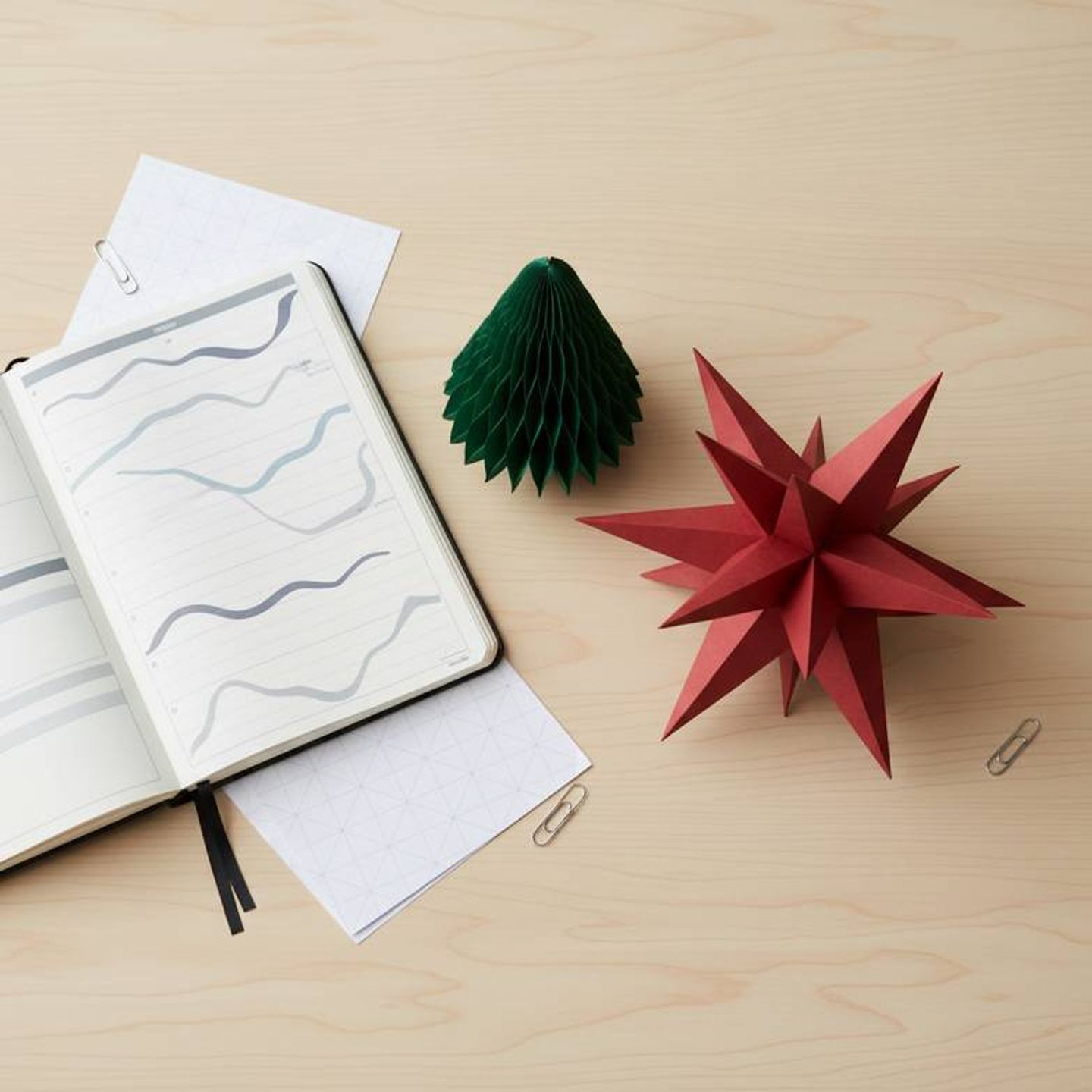 A detailed Christmas decoration sourcing timeline laid out on a planner with honeycomb paper ornaments nearby.