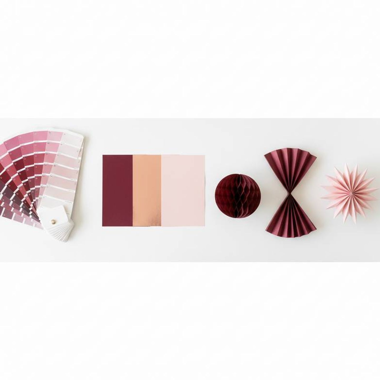 A Pantone color swatch book laid next to different samples of paper, showing the process of customizing colors for Valentine's Day paper decorations.