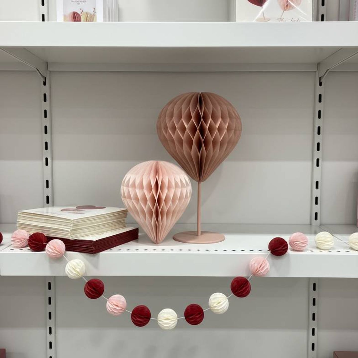 A mix of tabletop and hanging Valentine's Day paper decorations for retail on a store shelf, showing different sizes and shapes in a consistent color scheme.