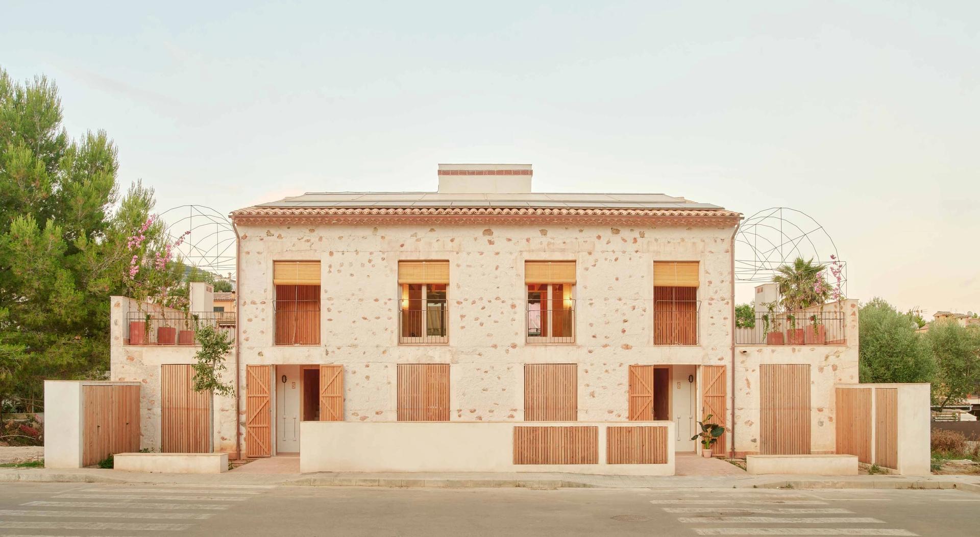 Main façade of the six social housing building Ses Veles in Puigpunyent with cyclopean wall and wooden shutters