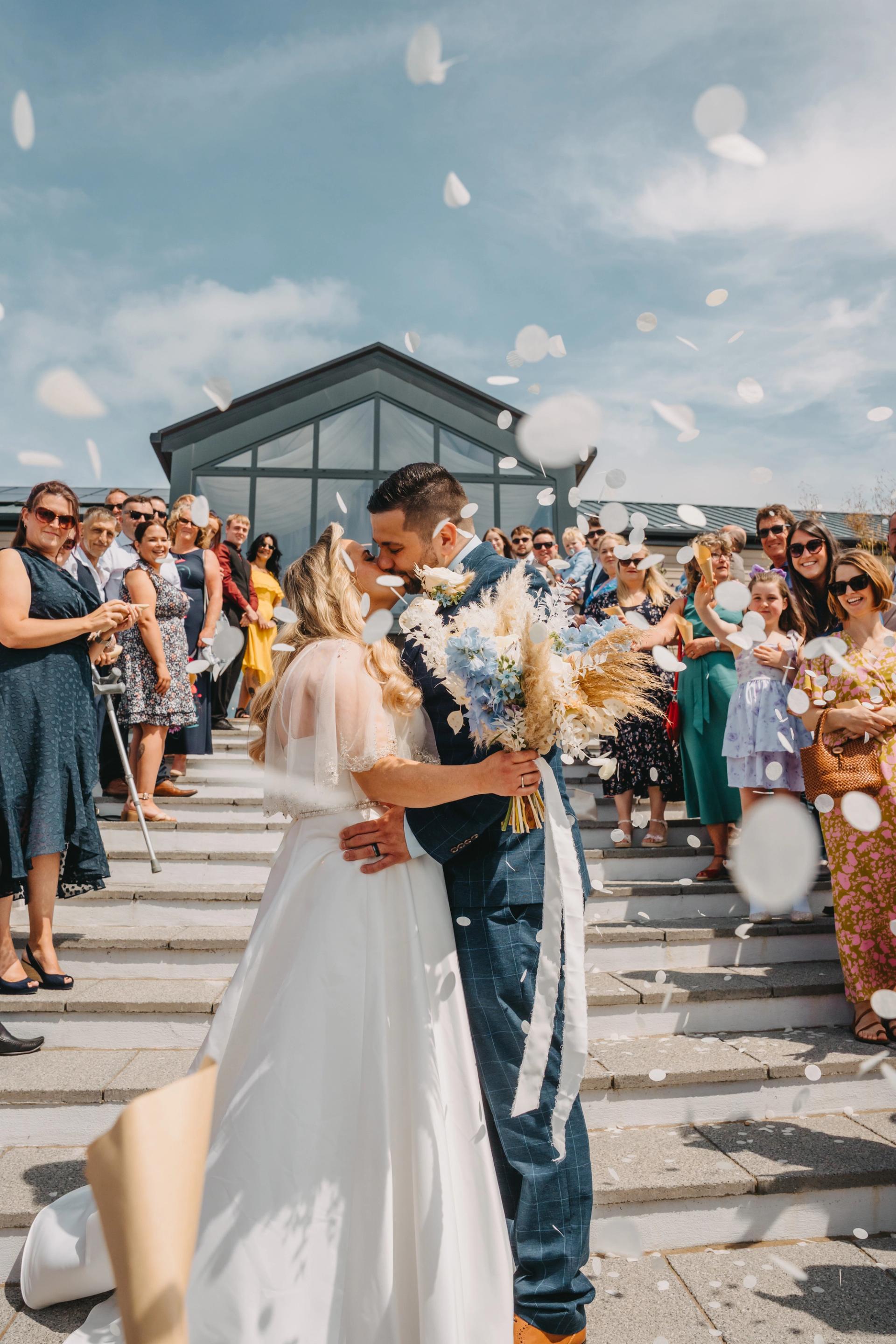 The happy couple kissing while guests throw confetti