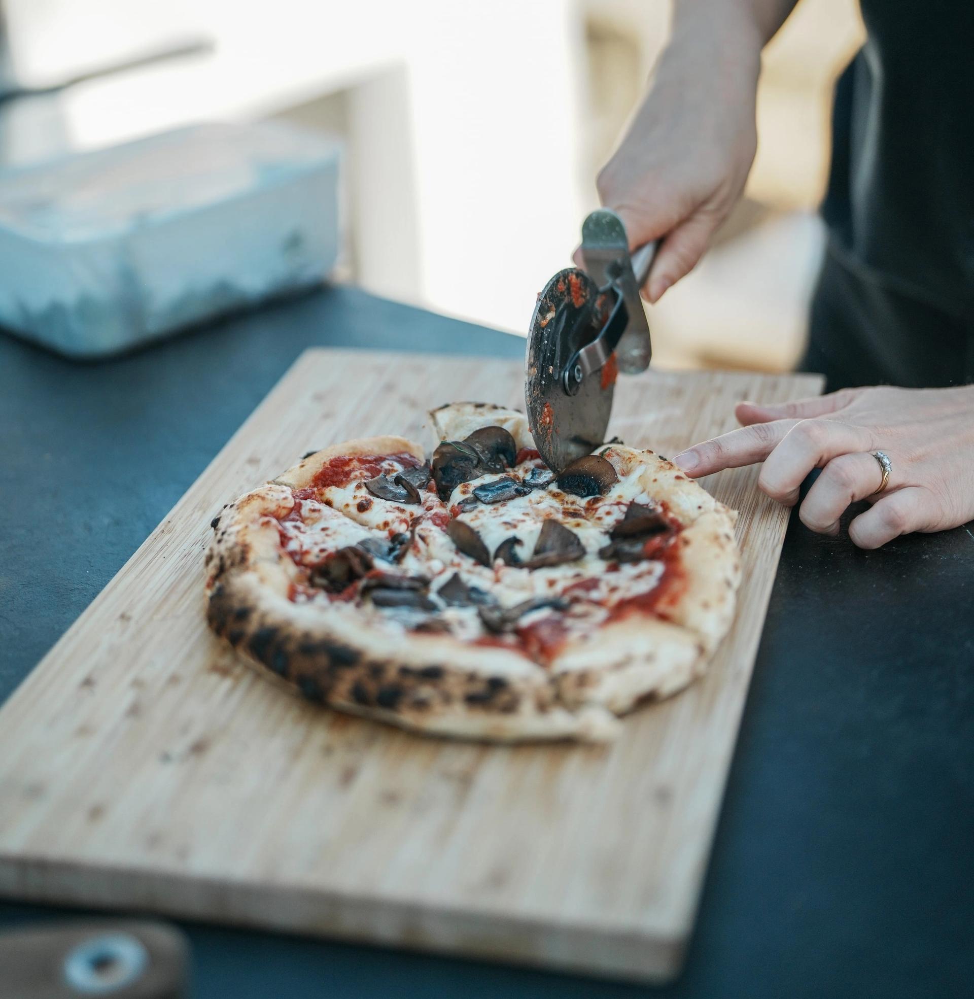A pizza being cut on a wooden chopping board