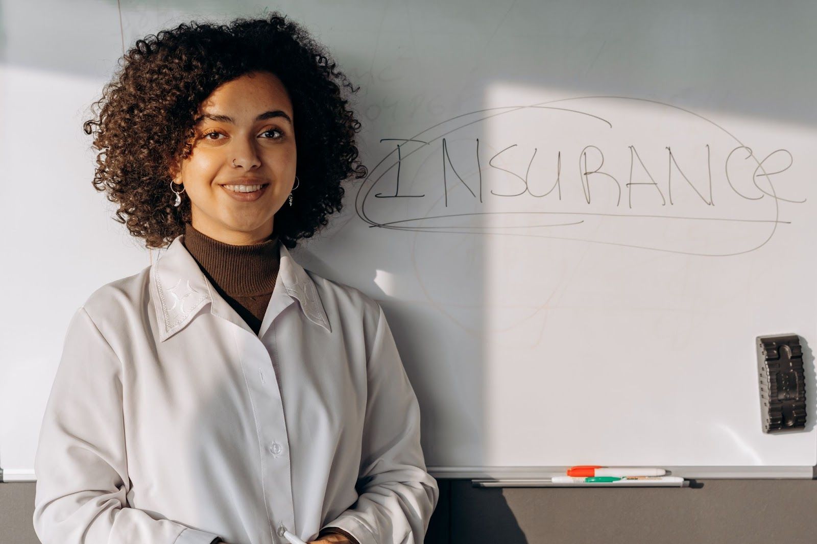 Insurance written on a whiteboard with a woman standing in front of it.