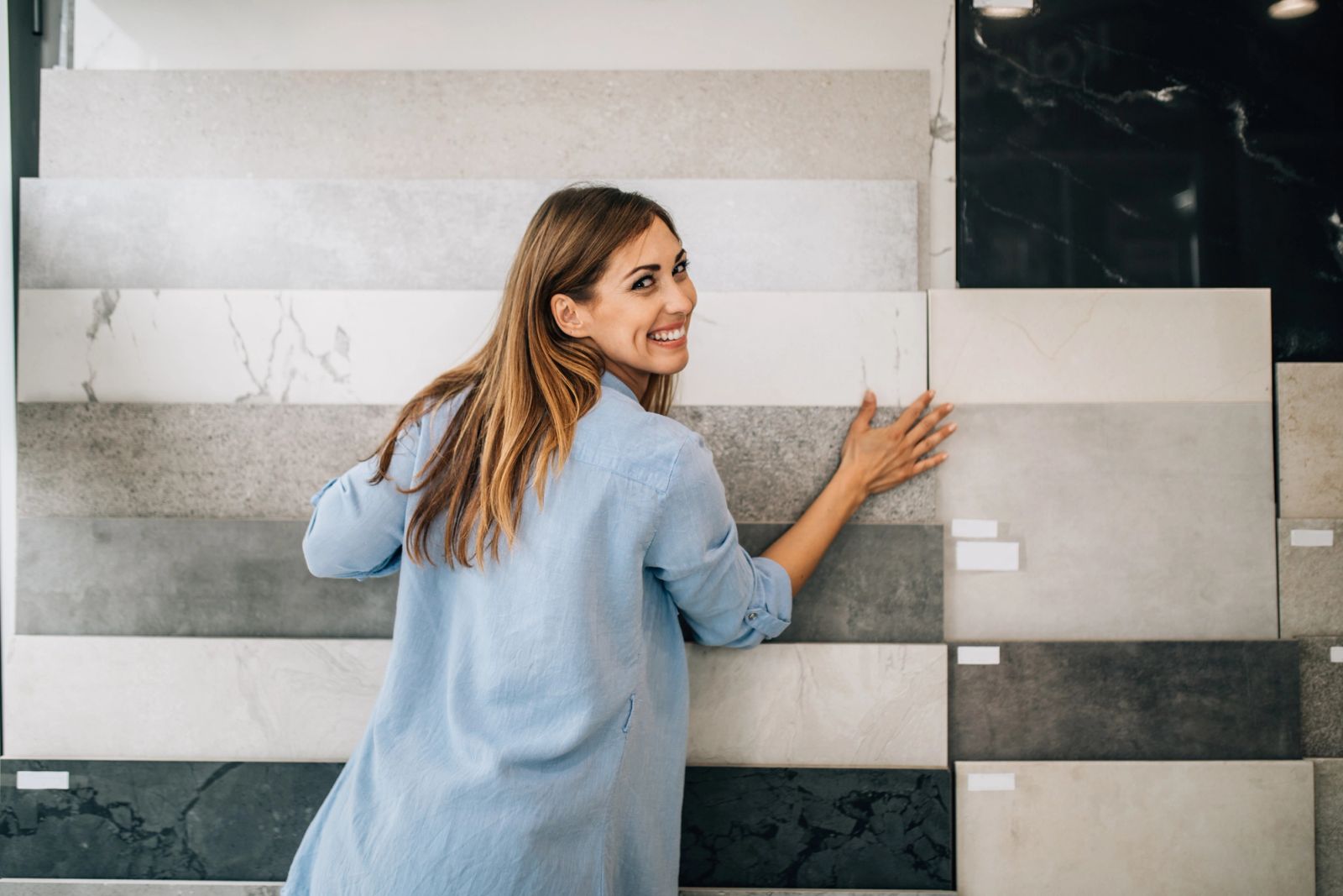 Woman comparing ceramic and stone tile samples in a flooring showroom while shopping for discounted flooring and overstock deals through FLRPL