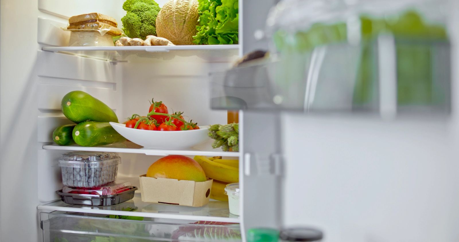Open refrigerator with fresh produce and groceries displayed on interior shelves in an appliance showroom