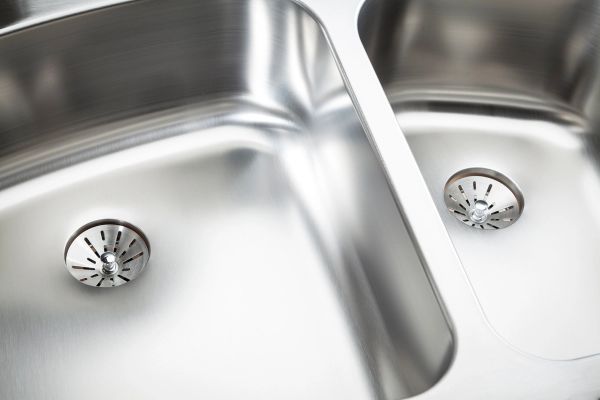 Double-basin stainless steel kitchen sink with modern drain strainers in a showroom display