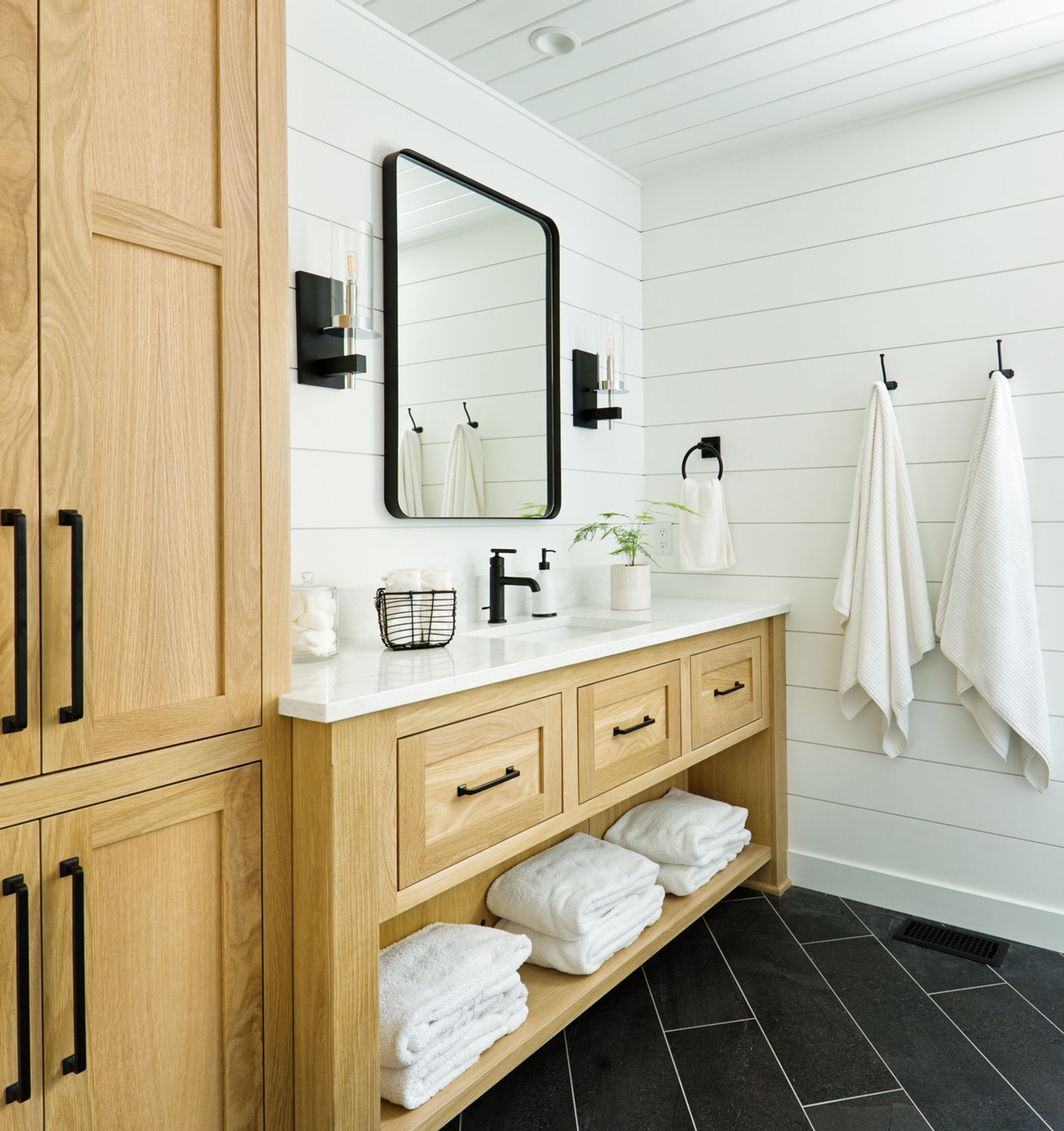 Floor model bathroom vanity with light wood cabinetry, white countertop, and black hardware in a showroom bathroom
